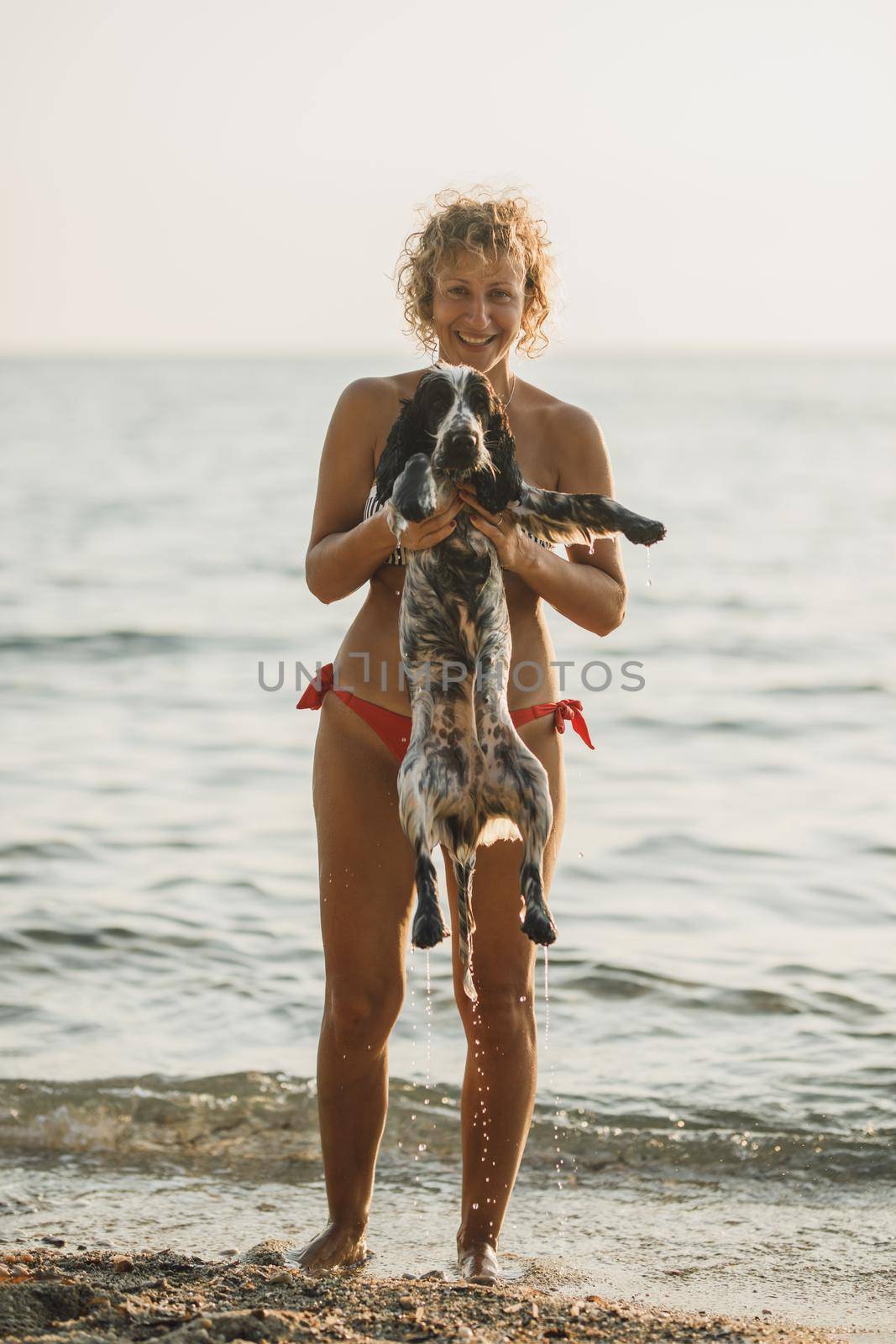 Young smiling woman having fun with her dog at the beach. 