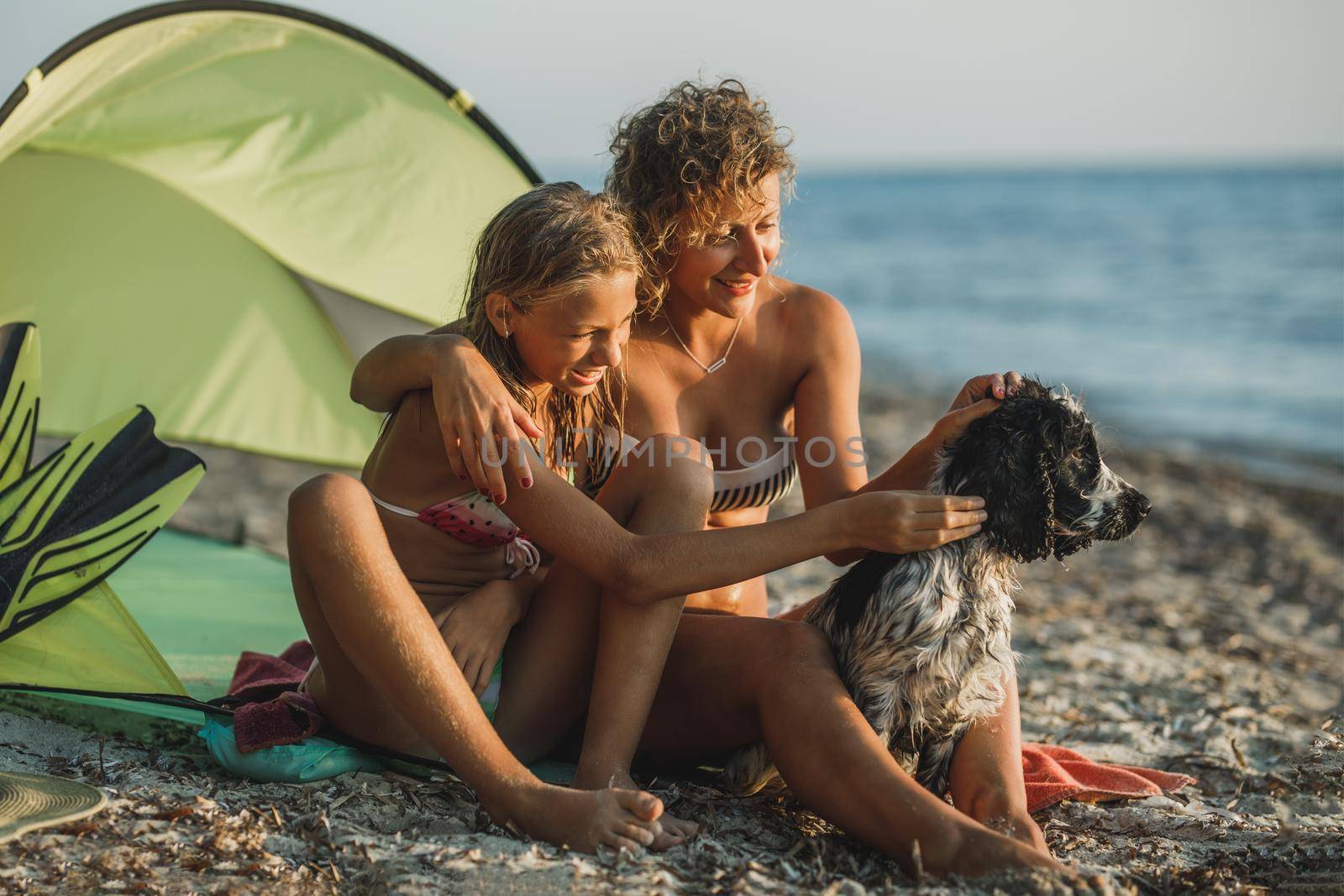 Young mom and her teen daughter spending day at the beach with their cute Cocker Spaniel dog. 