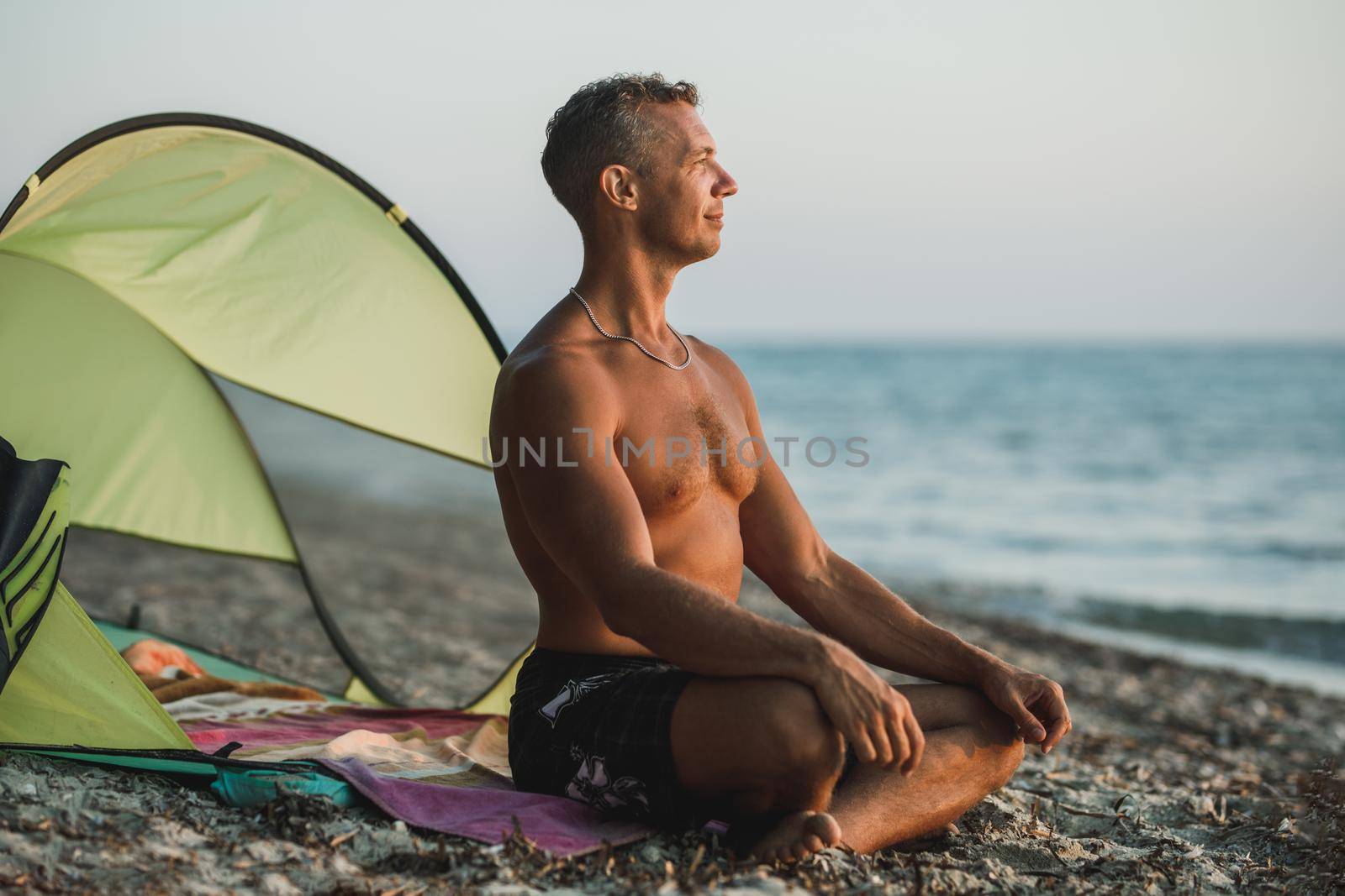 A handsome man relaxing and watching the sun go down at the beach.