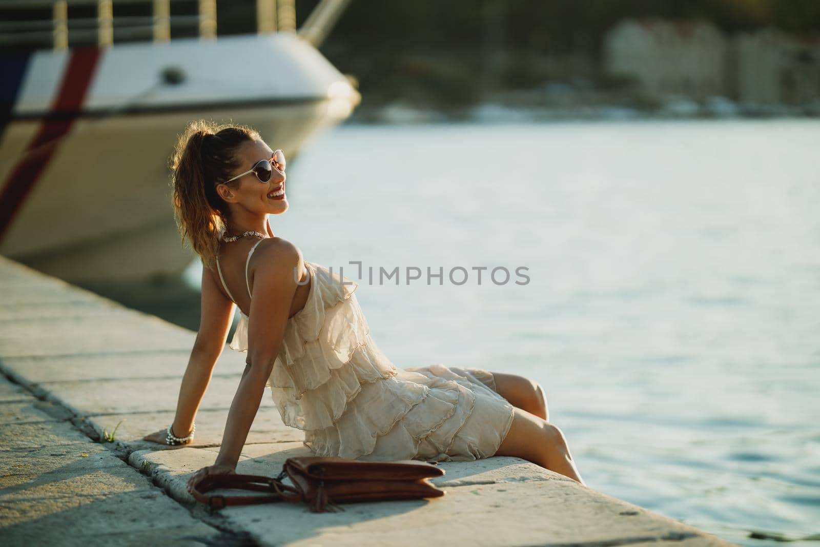 Young happy woman sitting near the seaside while enjoying a summer vacation.