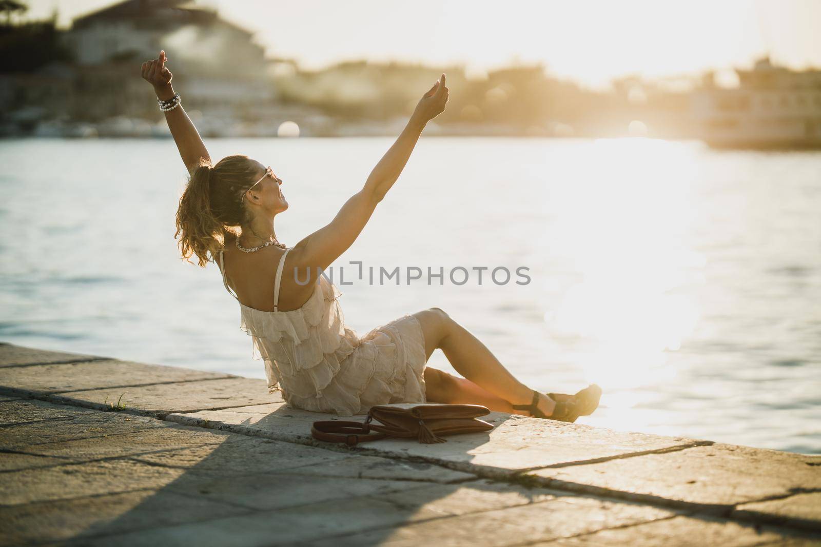 Young happy woman sitting near the seaside while enjoying a summer vacation.