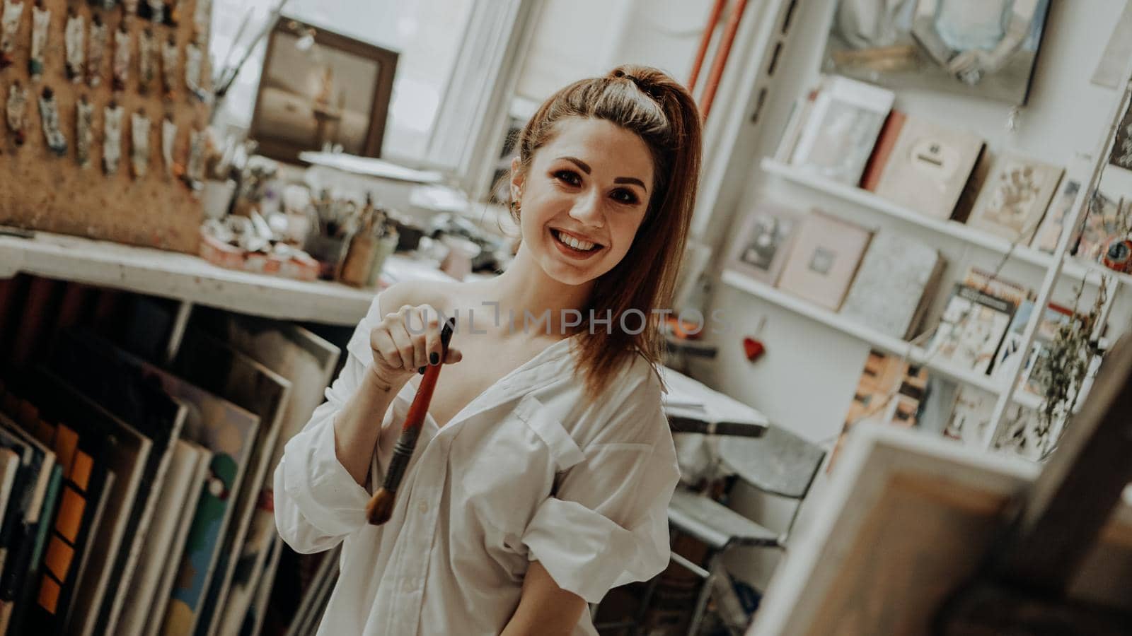 Portrait of happy smiling female artist with brush in art workshop. Selective focus. Vintage style photo