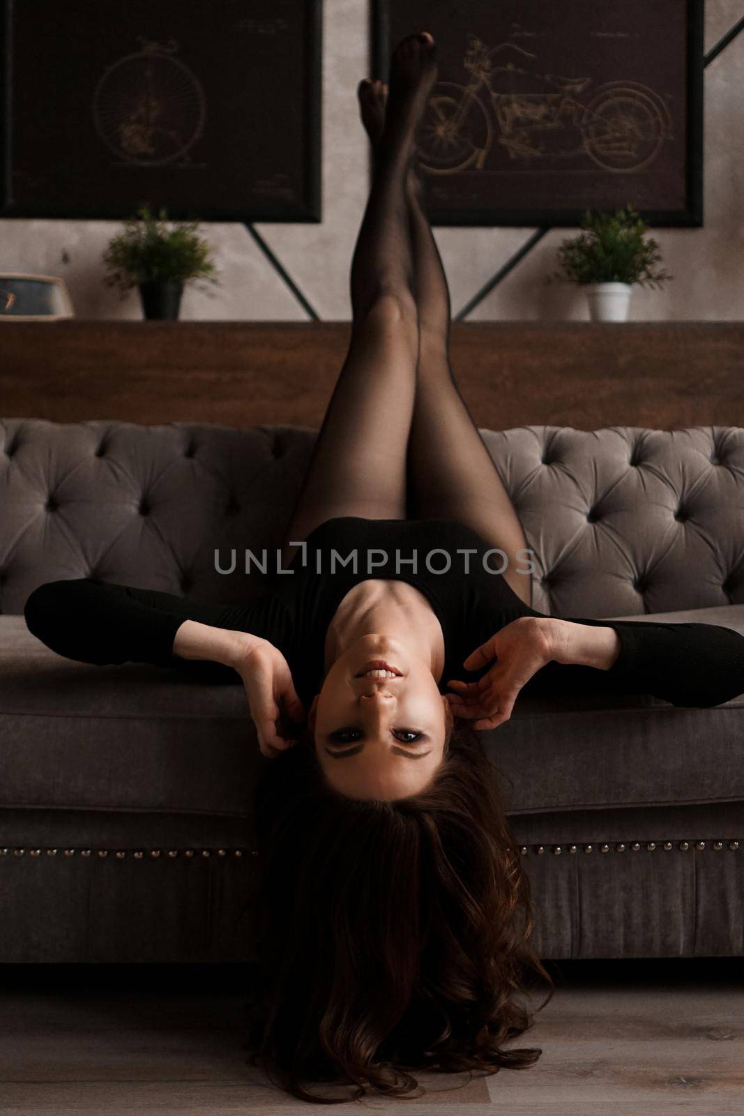 Beautiful young woman in a black transparent pantyhose on a couch - loft room