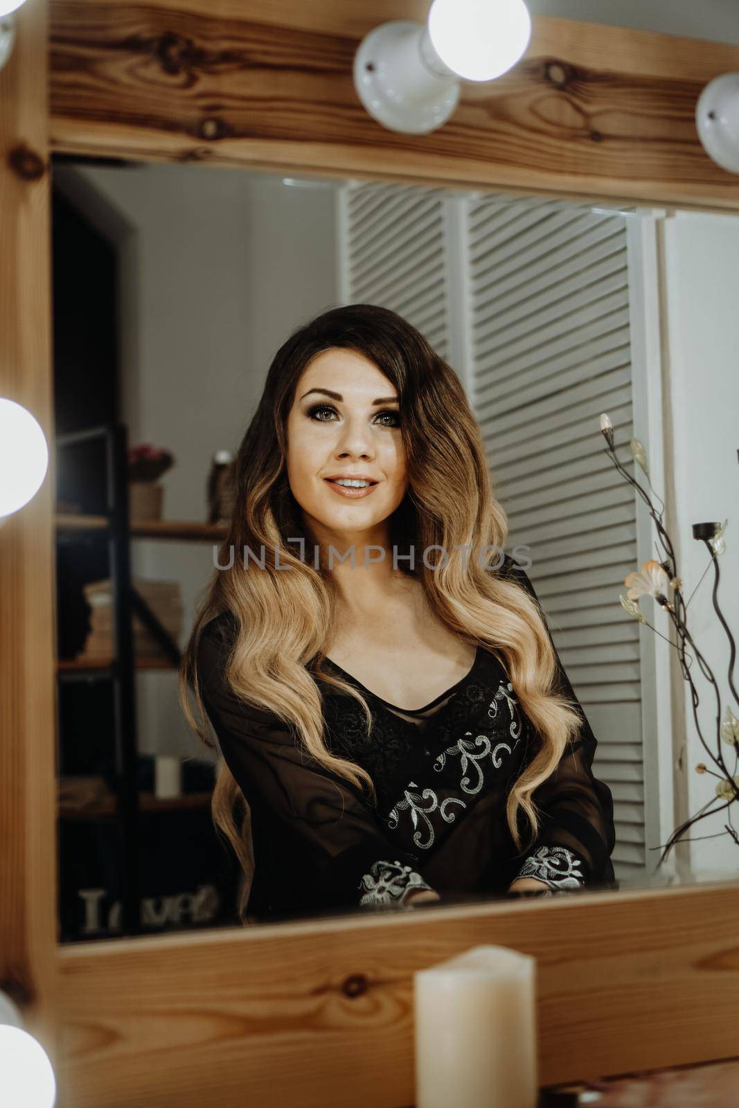 Beautiful young woman looking at her reflection in a dressing room mirror. Happy glamorous woman