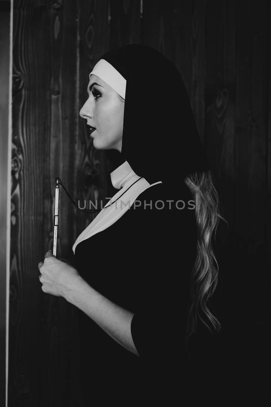 Sexy nun prays indoor . Beautiful young holy sister. Young beautiful nun with a cross in a robe in a black interior. Black and white