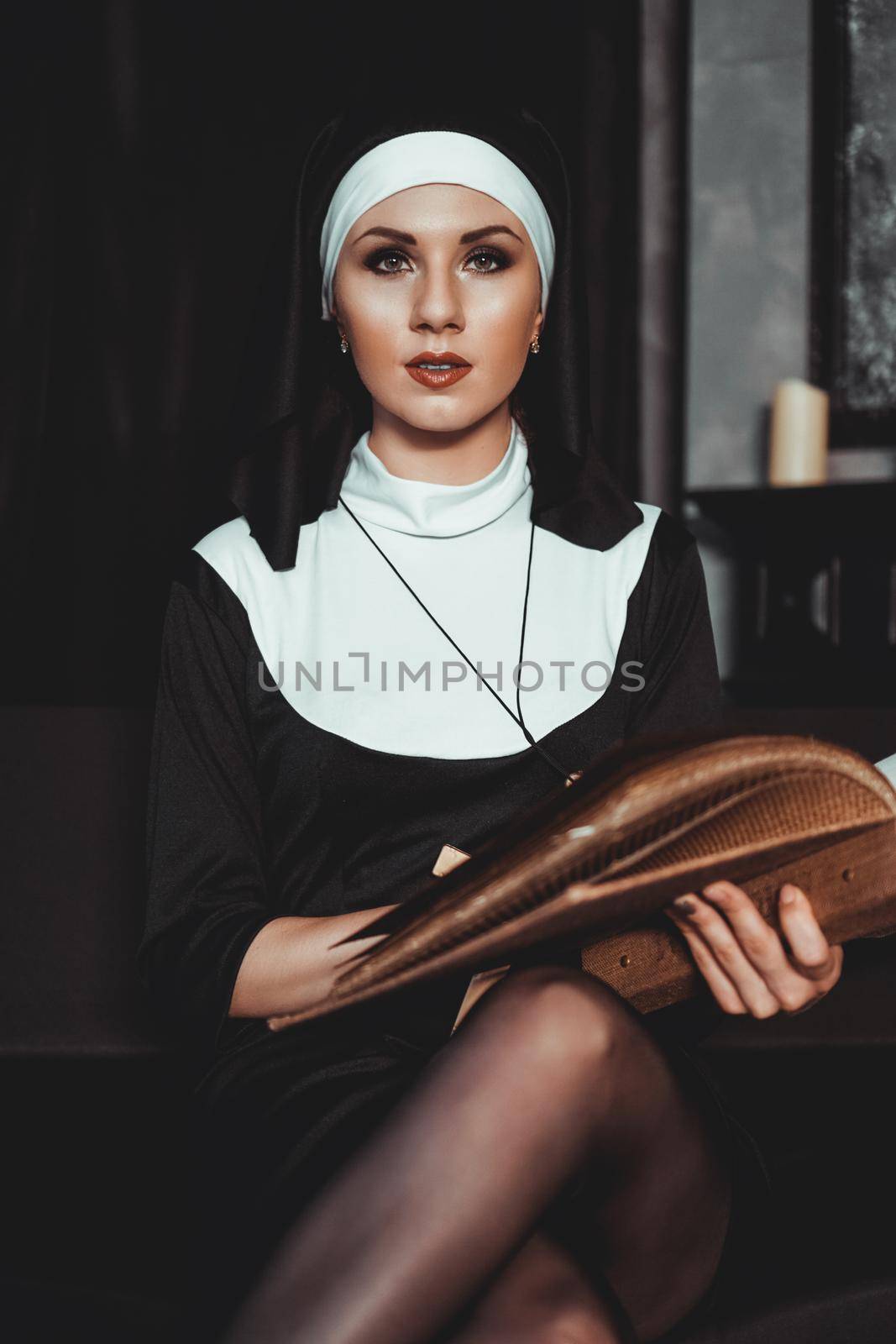 Beautiful young nun in religion black suit holds Bible and posing on camera with big book on a black background. Religion concept.