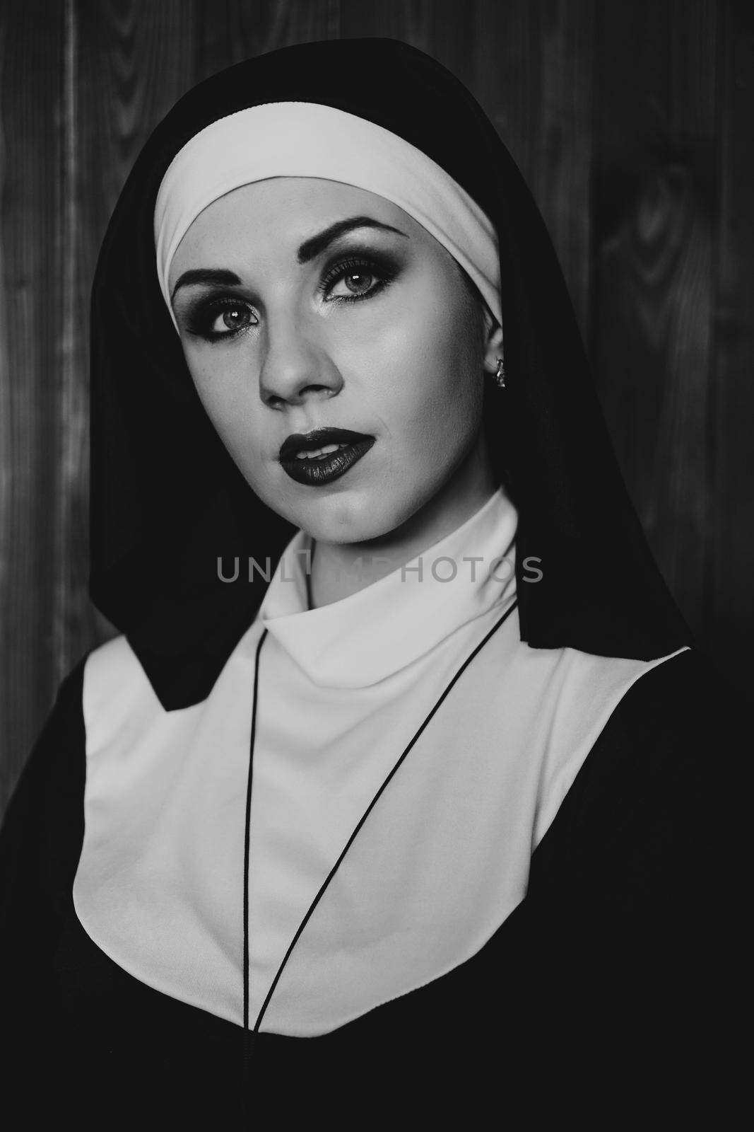 Sexy nun prays indoor . Beautiful young holy sister. Young beautiful nun with a cross in a robe in a black interior. Black and white