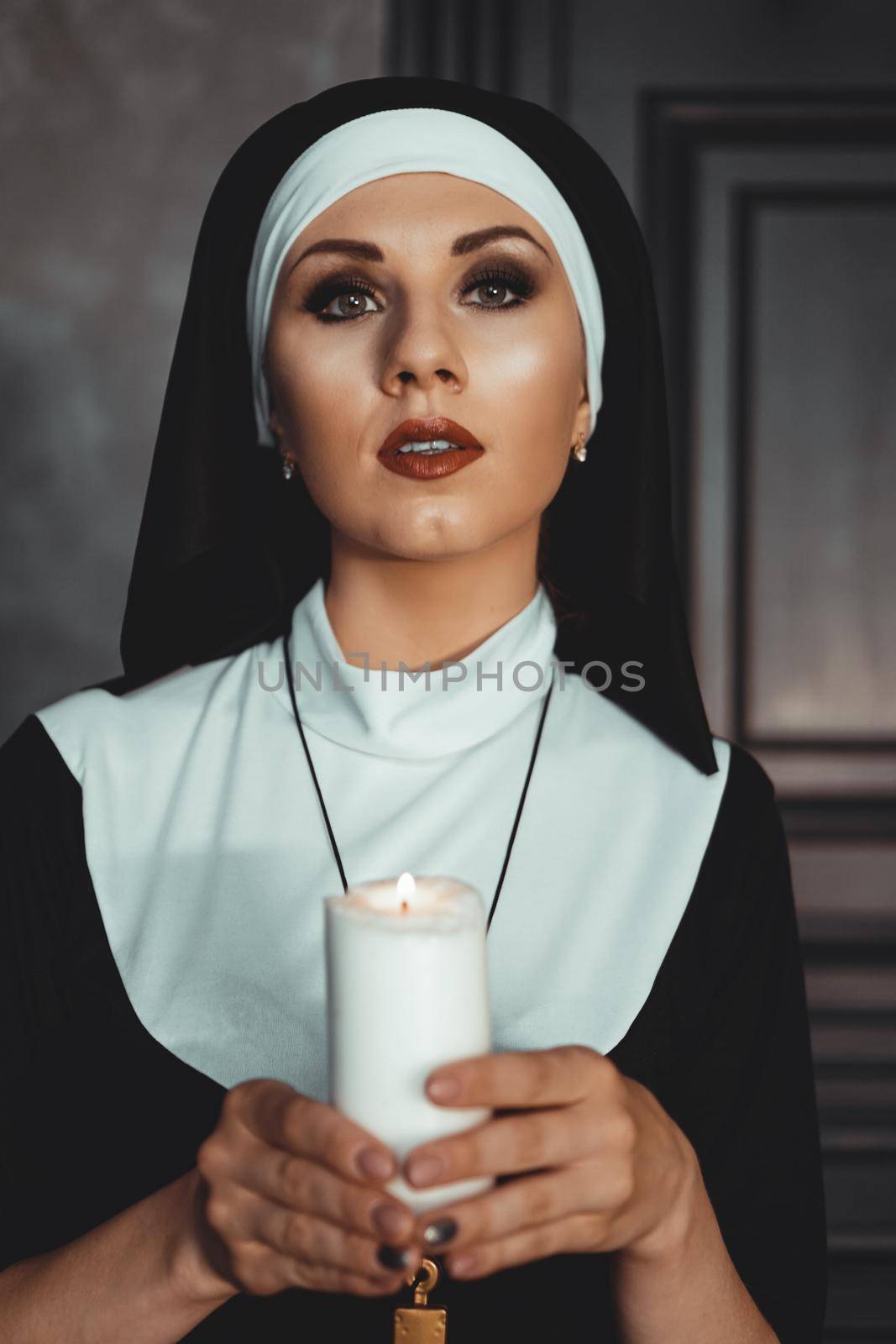 Young catholic nun is holding candle in her hands. Photo on black background by natali_brill