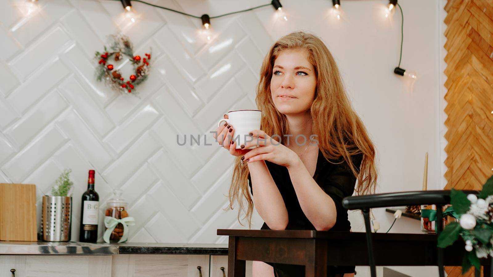 Woman holds a cup of coffee in the morning in Christmas kitchen. Happy young woman having fun and smiling
