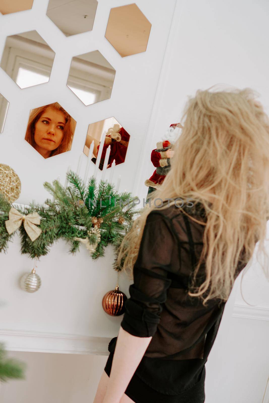 A pretty blonde hair woman in Christmas time stands near the mirror. Winter spirit. Happy New Year