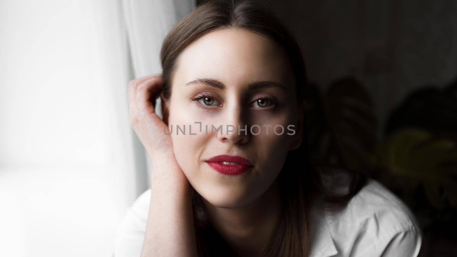 Portrait of attractive brunette woman. Home portrait of a woman with red lips in a white shirt