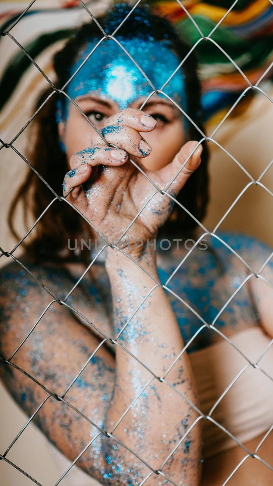 Brunette girl behind the net. Portrait of beautiful woman with blue sparkles on her face. The concept of people with Individuality