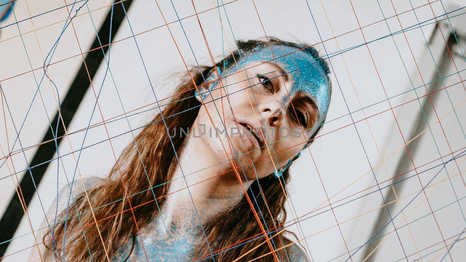 Brunette girl behind the threads net. Portrait of woman with blue sparkles by natali_brill