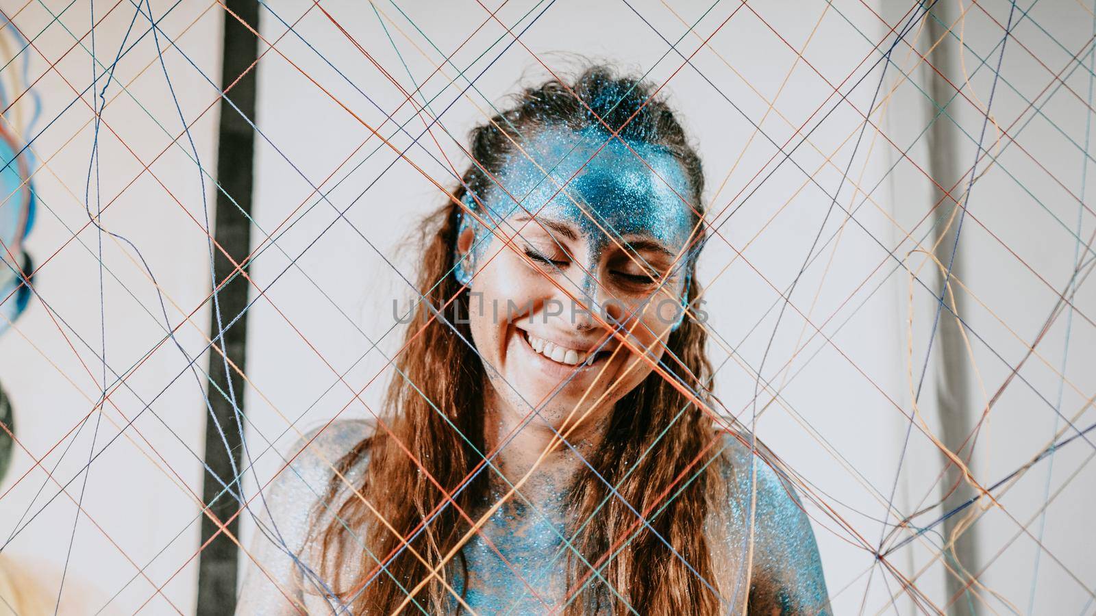Brunette girl behind the threads net. Portrait of beautiful woman with blue sparkles on her face. The concept of people with Individuality