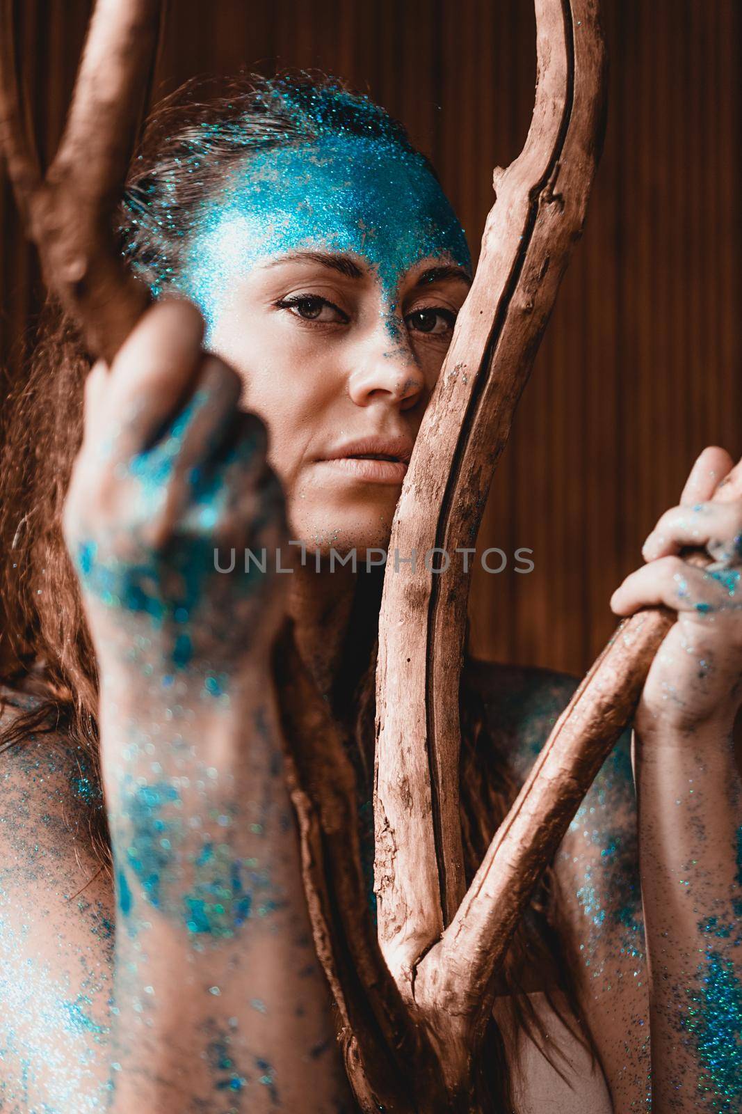 Portrait of a beautiful woman posing like in the wild forest. Woman with blue sparkles on her face. People are different from others. Individuality