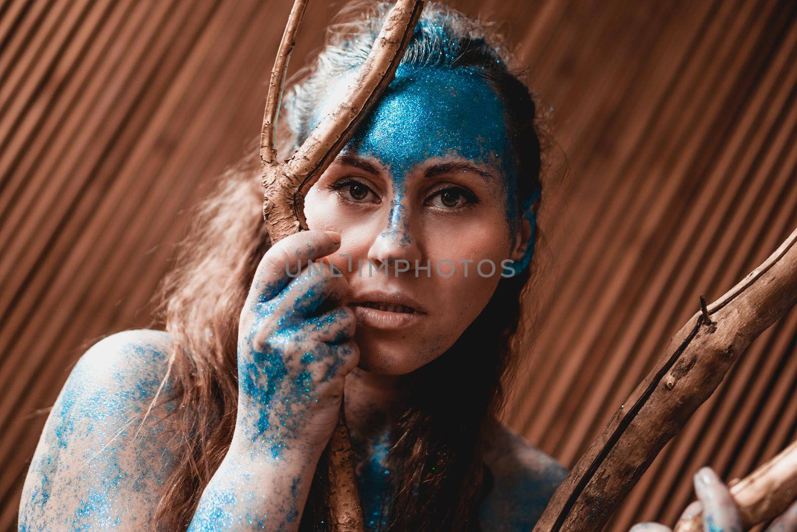 Portrait of a beautiful woman posing like in the wild forest. Woman with blue sparkles on her face. People are different from others. Individuality
