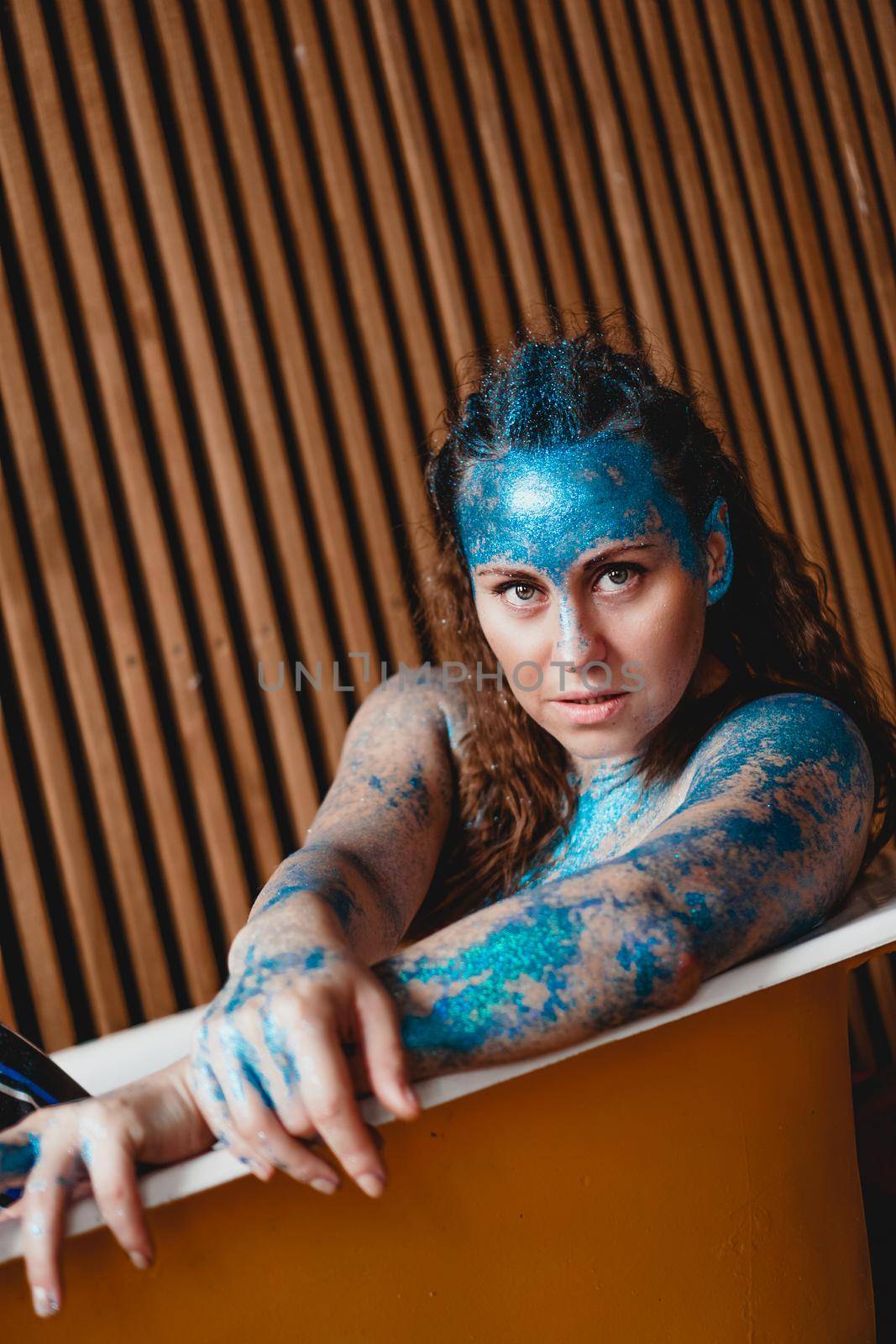 Portrait of beautiful woman with blue sparkles on her face in the bath. The concept of Individuality