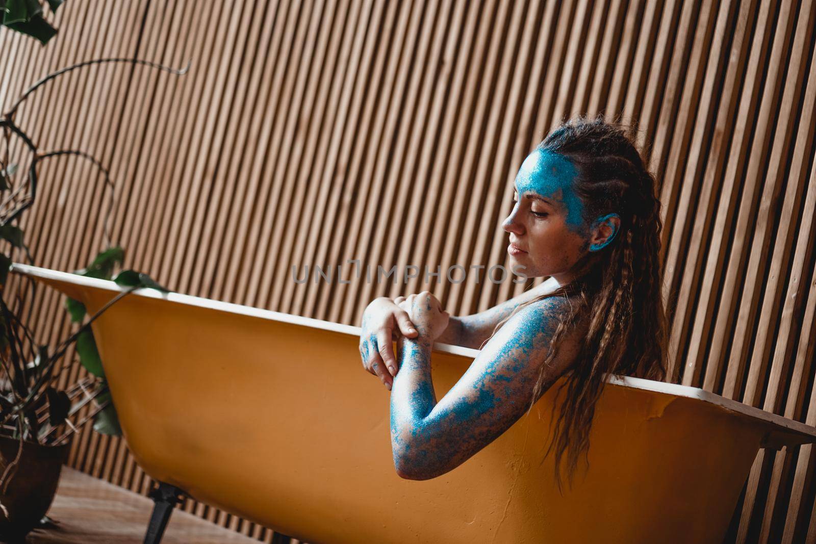 Portrait of beautiful woman with blue sparkles on her face in the bath. The concept of Individuality