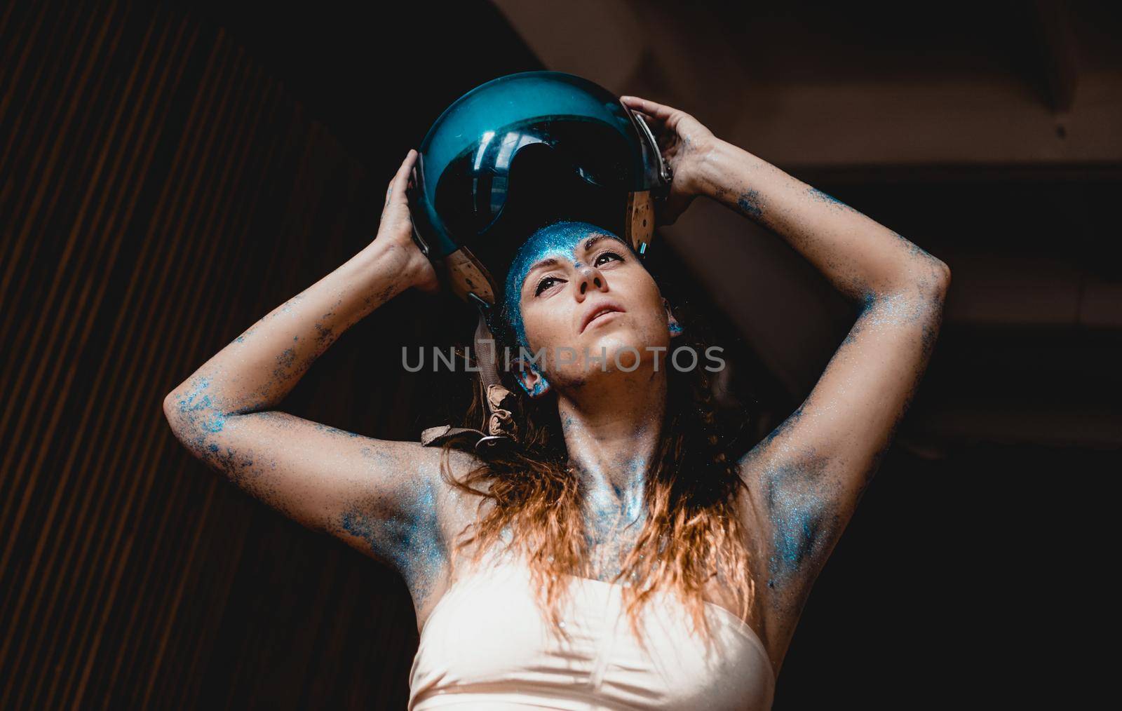 Woman motorcyclist put on crash helmet. Woman with blue sparkles on her face. by natali_brill