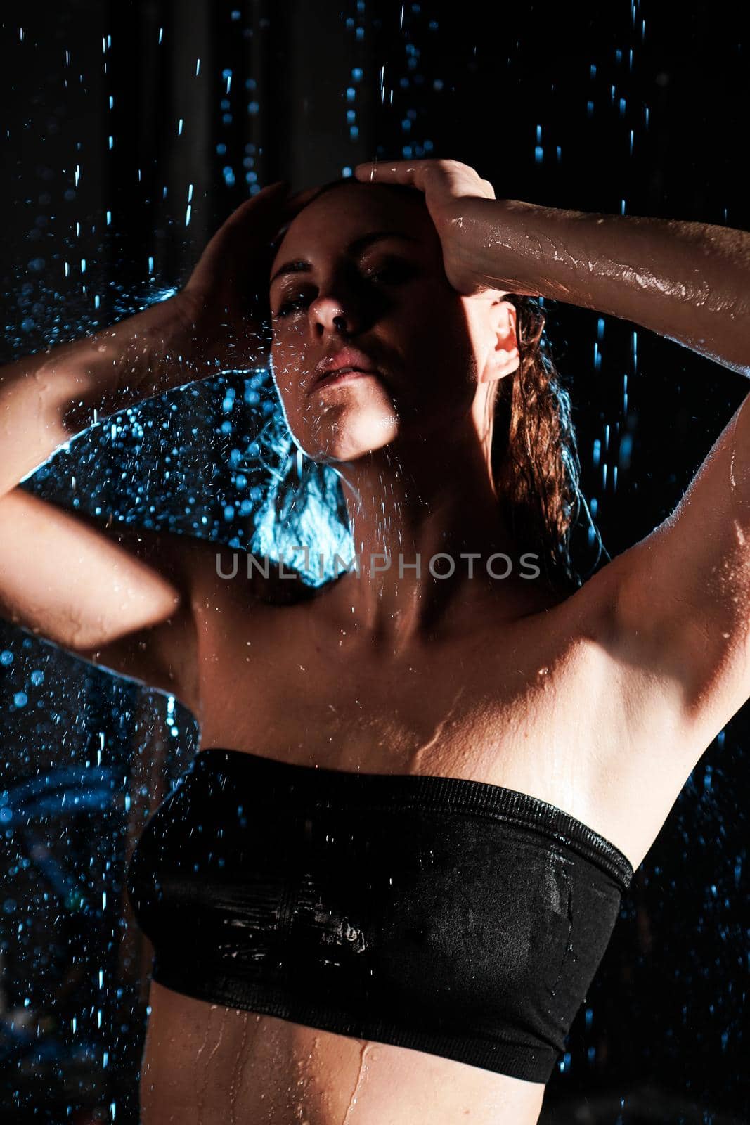Wet beautiful woman under the falling drops of rain - photo in studio with blue light