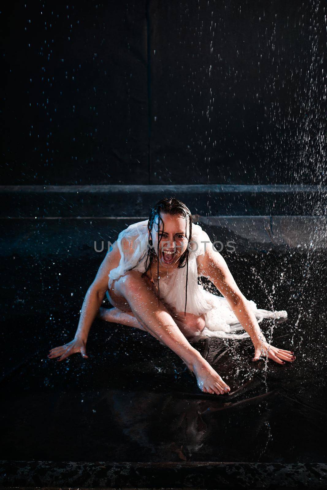 Beautiful woman in aqua in transparent fabric in neon light. The girl under the raindrops screams in despair. Emotional photo