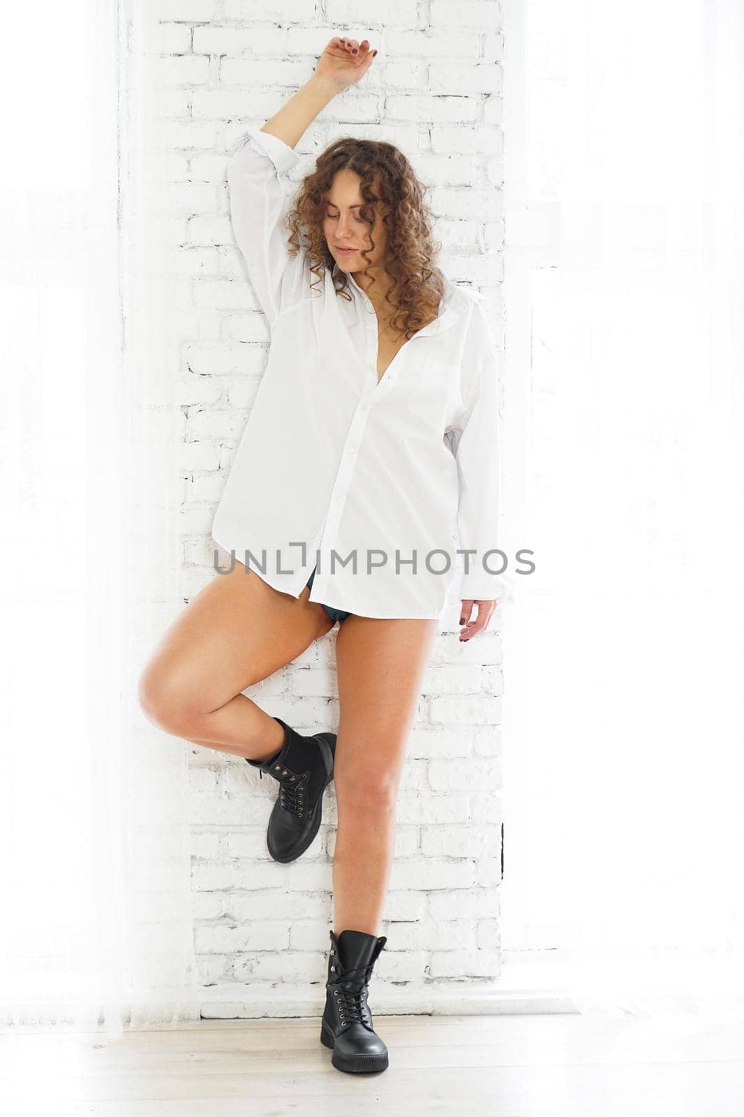 Studio portrait of pretty sexy woman model with beautiful long legs standing near brick white wall