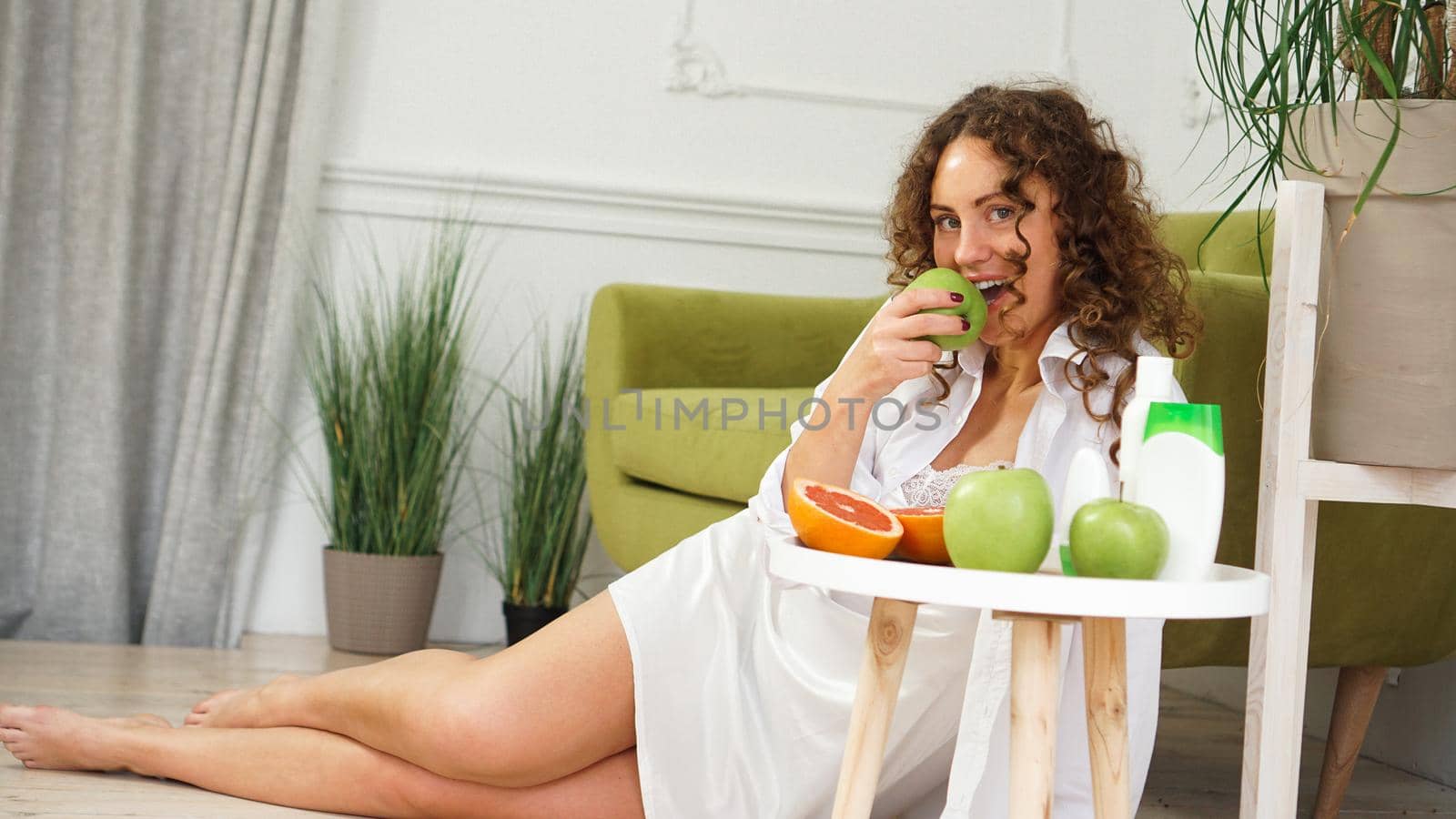 Young woman eating green apple at home. Healthy nutrition, diet food concept. Close-up portrait of beautiful young woman eating organic green apple.