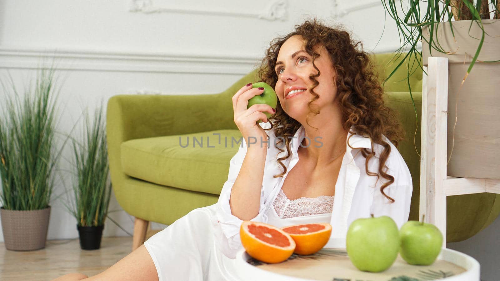 Young woman eating green apple at home. Healthy nutrition, diet food concept. Close-up portrait of beautiful young woman eating organic green apple.