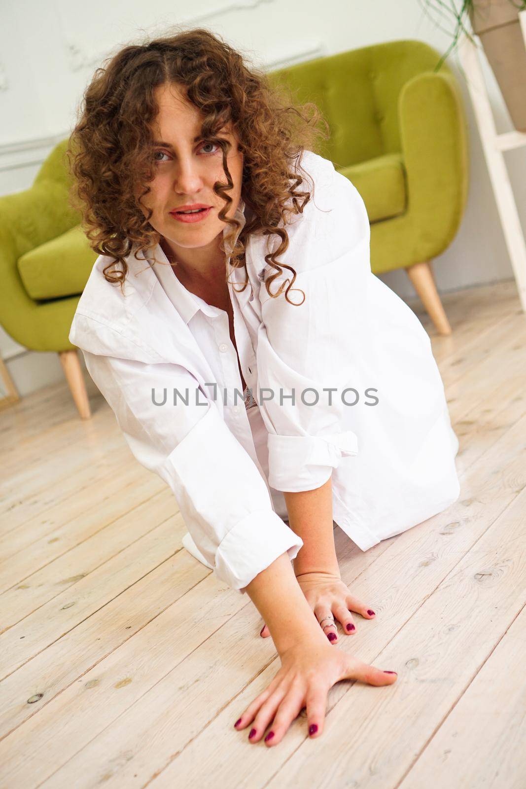Sexy woman in white shirt on wooden floor - Portrait of pretty middle-aged woman with curly hair at home - light room.