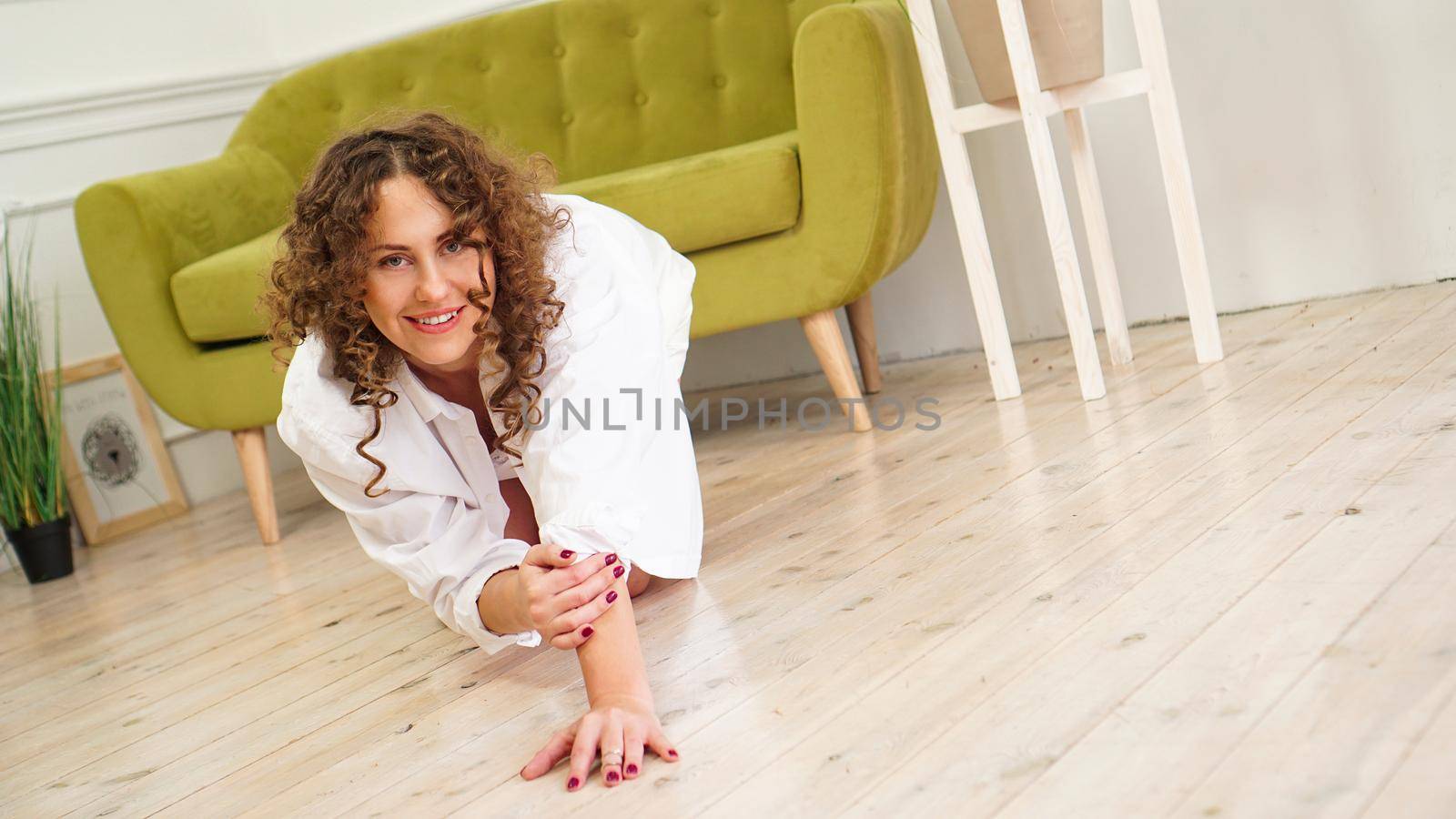 Sexy woman in white shirt on wooden floor - Portrait of pretty middle-aged woman with curly hair at home - light room.