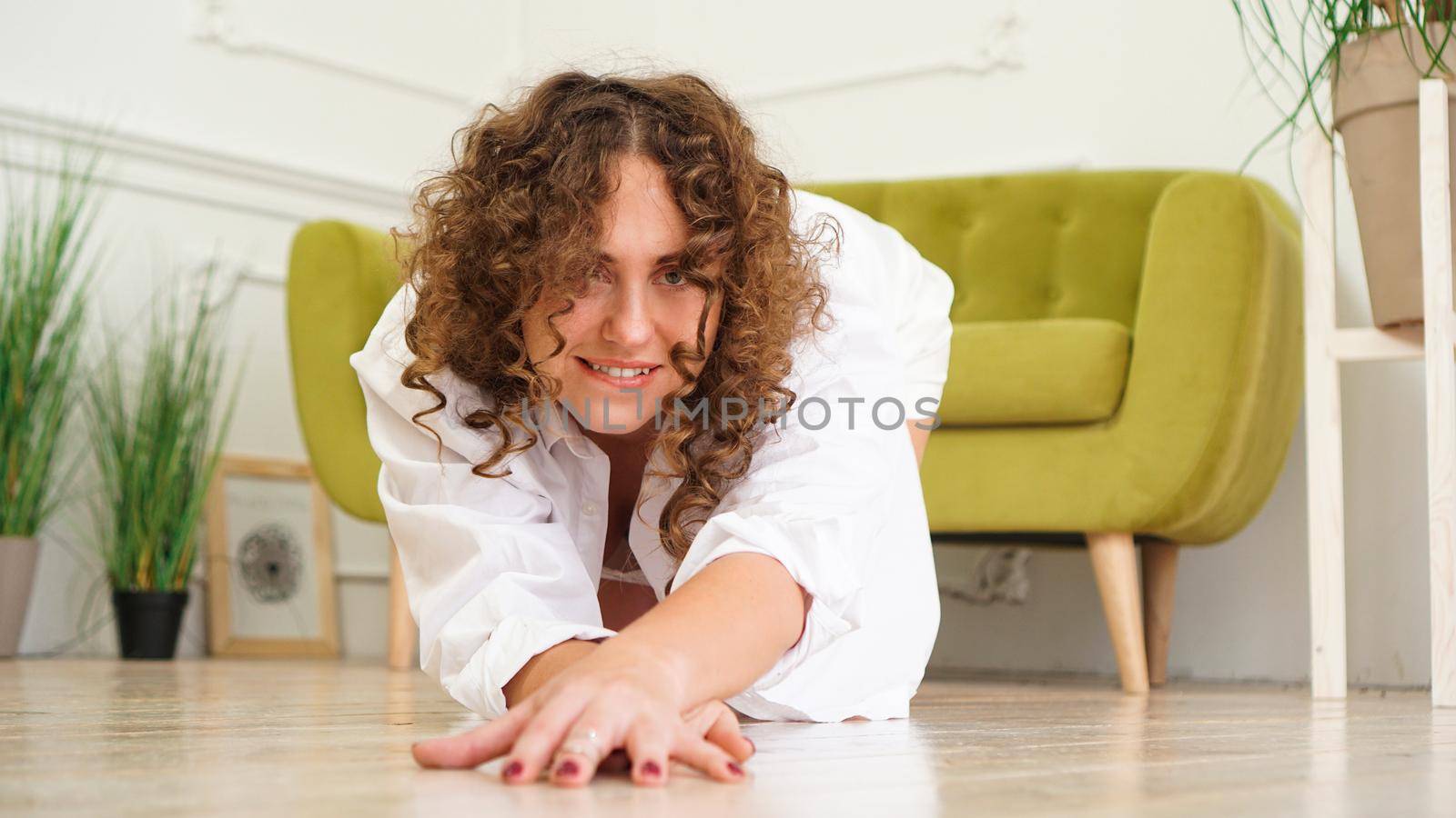 Sexy woman in white shirt on wooden floor - Portrait of pretty middle-aged woman with curly hair at home - light room.