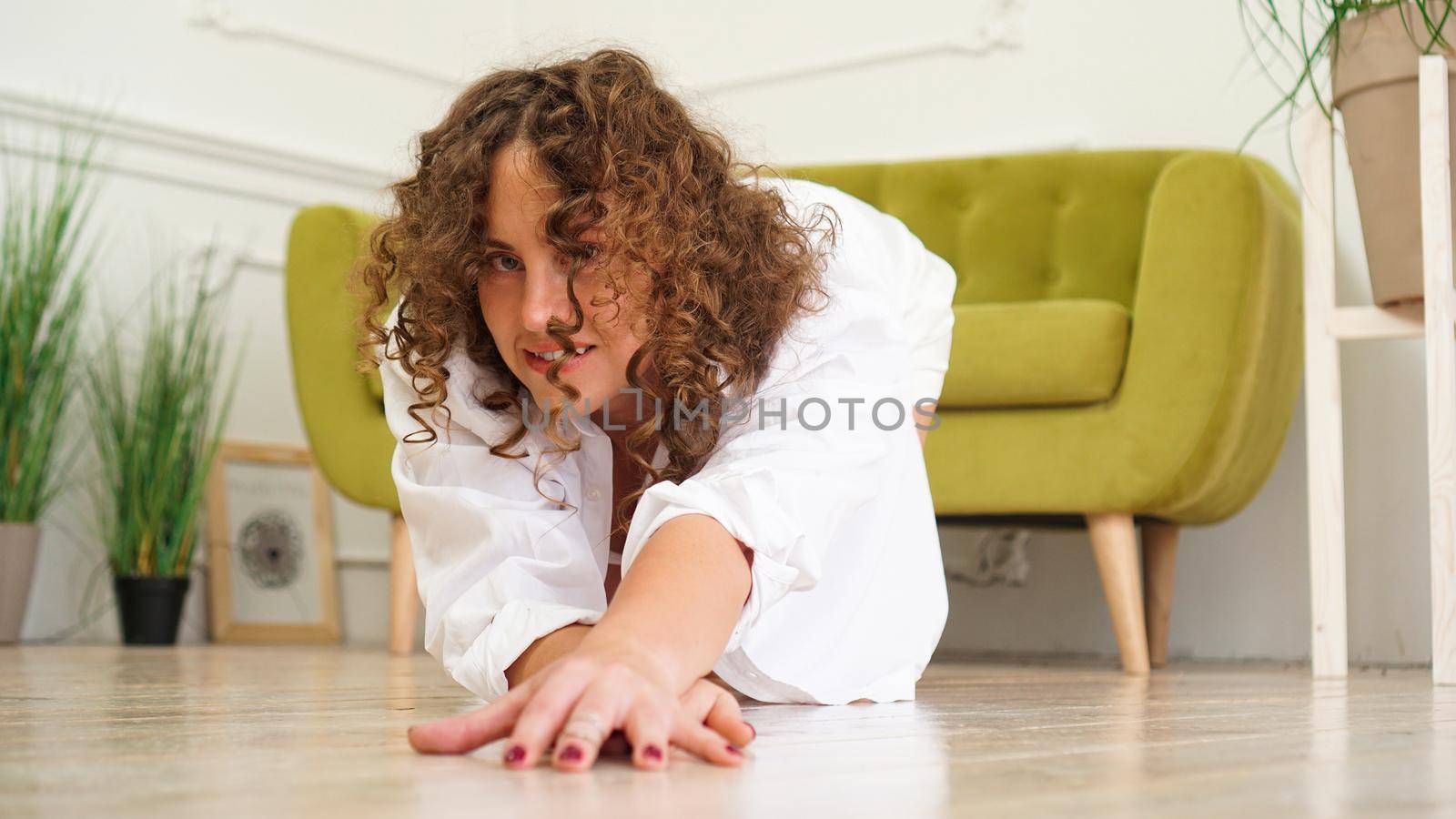 Sexy woman in white shirt on wooden floor - Portrait of pretty middle-aged woman with curly hair at home - light room.