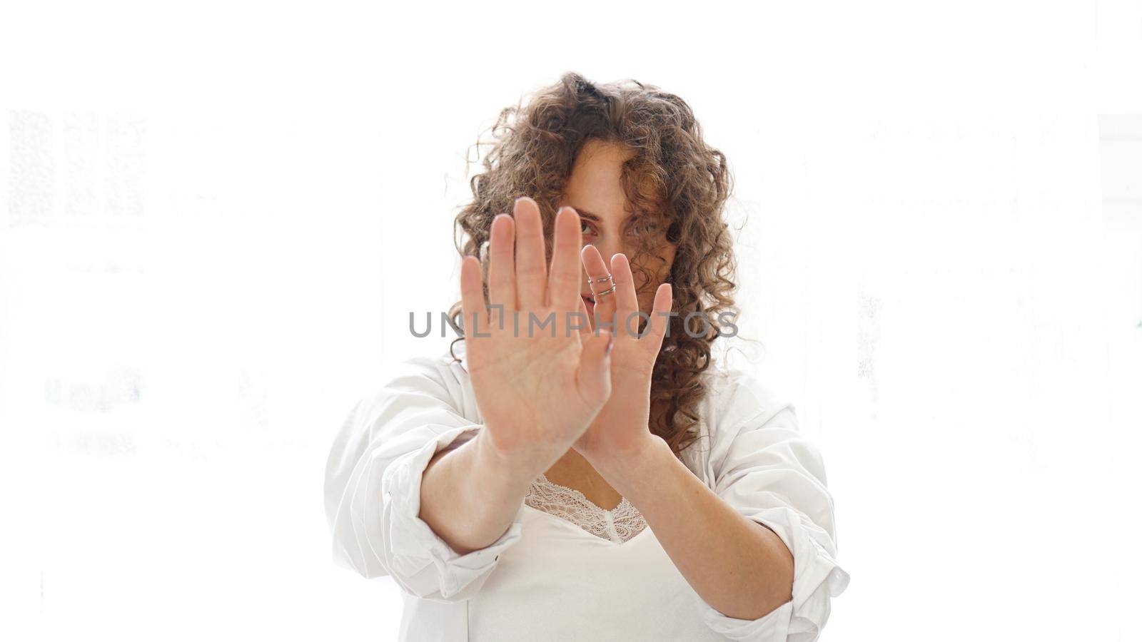 Woman making stop gesture with her hand isolated on a white background. Beautiful woman with curly hair in white lingerie at home