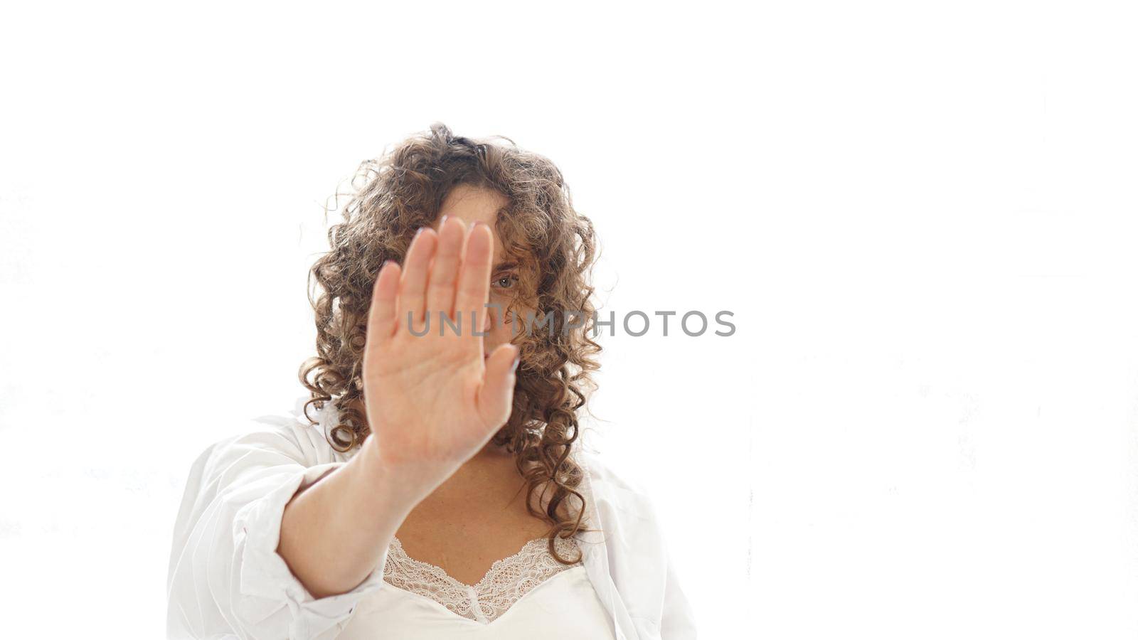 Woman making stop gesture with her hand isolated on a white background. Beautiful woman with curly hair in white lingerie at home