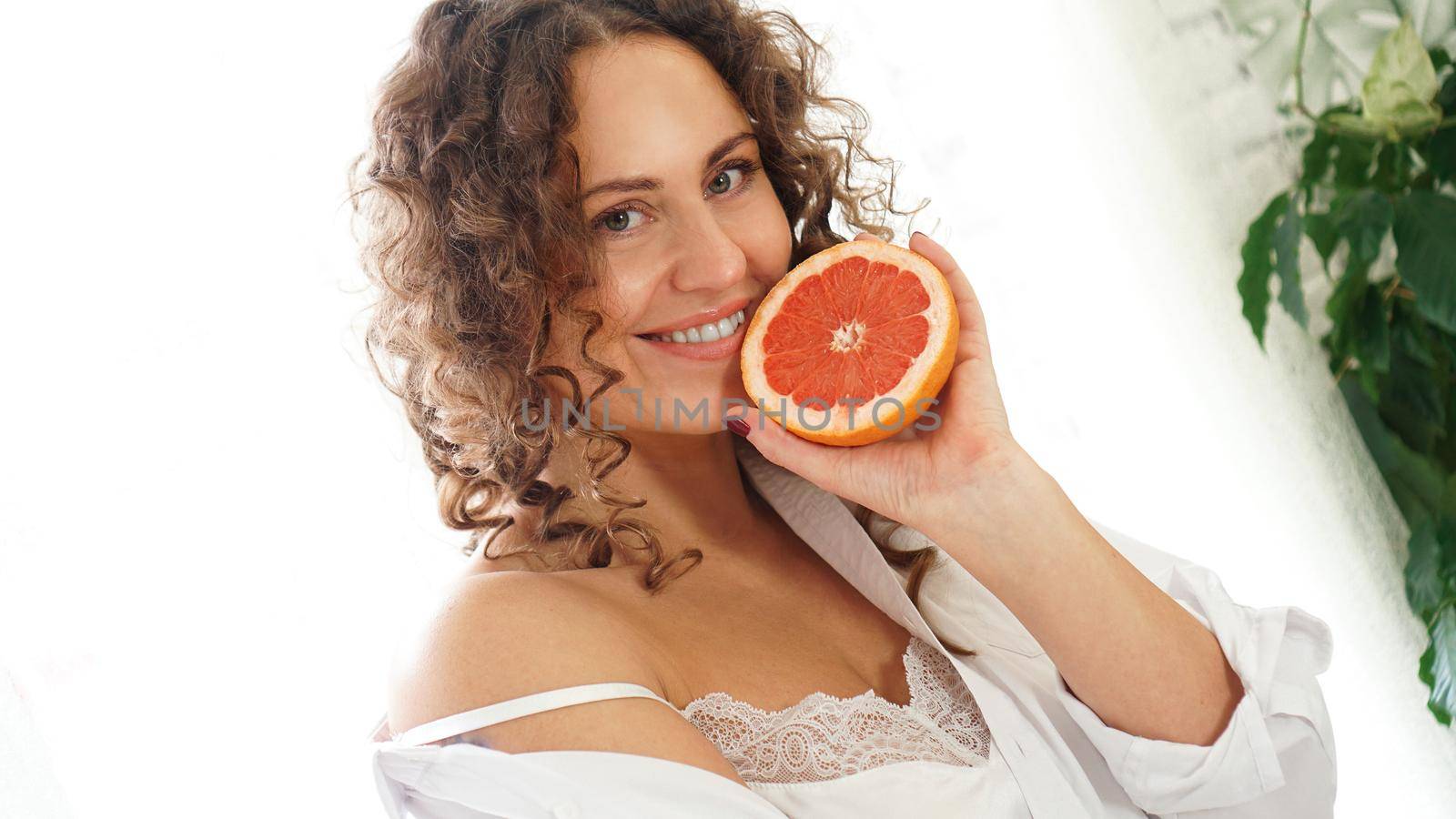 Portrait of pretty middle-aged woman with curly hair with grapefruit by natali_brill