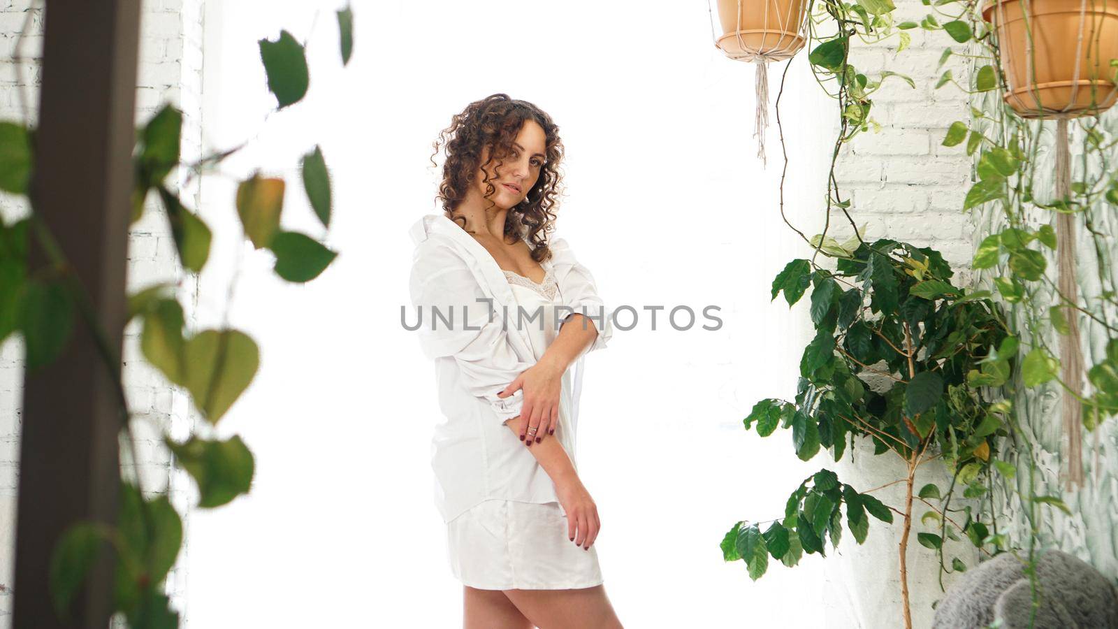 Sexy young woman in white shirt in bedroom with green plants by natali_brill