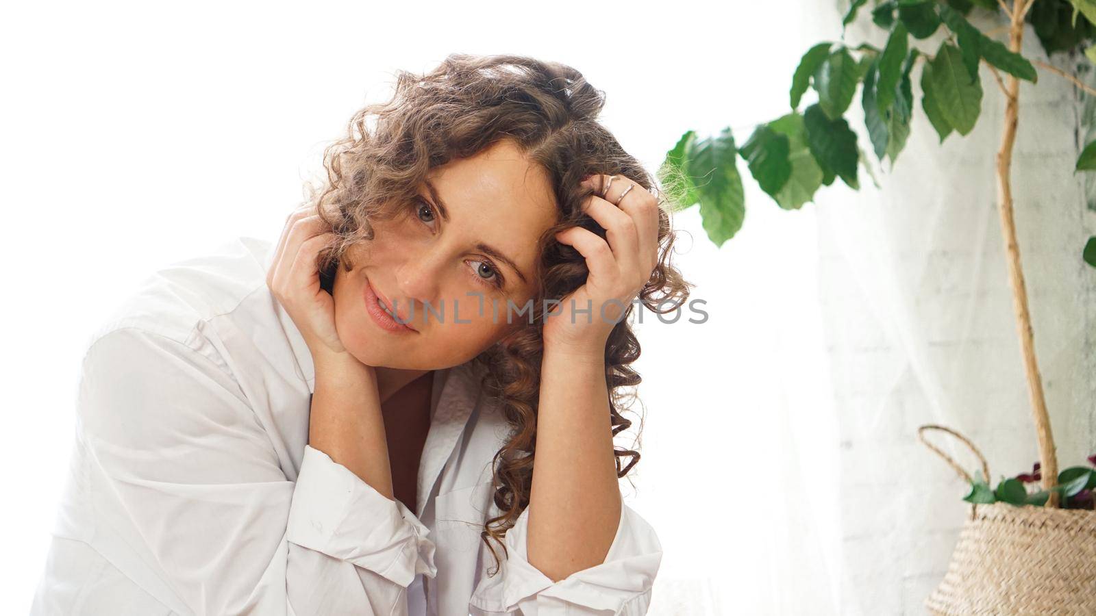 Portrait of a beautiful woman sitting at home with plants and smiling at camera. Happy morning - sunny day