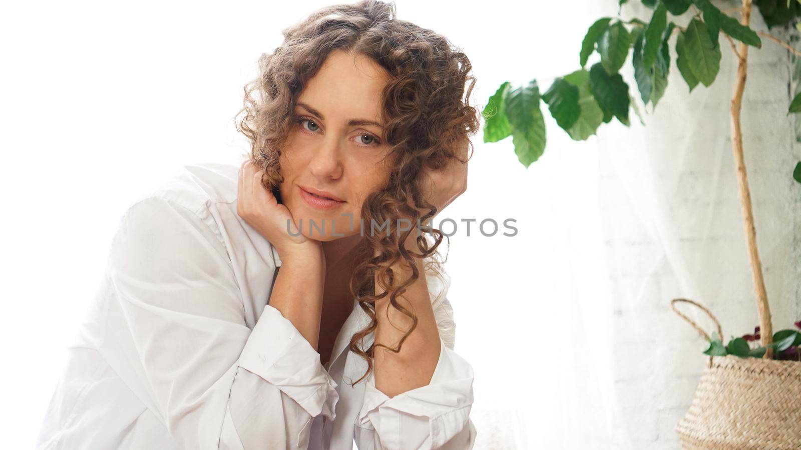 Portrait of a beautiful woman sitting at home with plants and smiling at camera by natali_brill