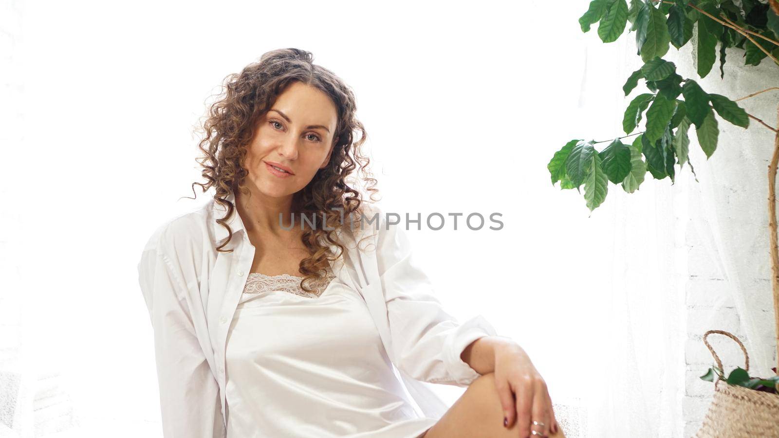 Portrait of a beautiful woman sitting at home with plants and smiling at camera. Happy morning - sunny day