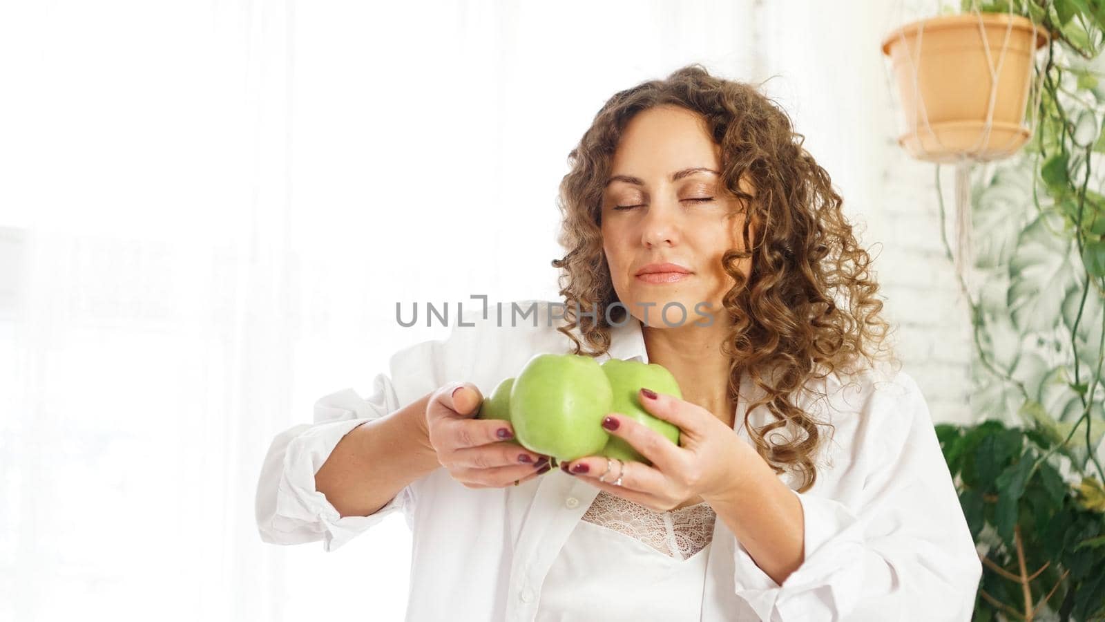 Beautiful young woman with curly hair smelling green apples