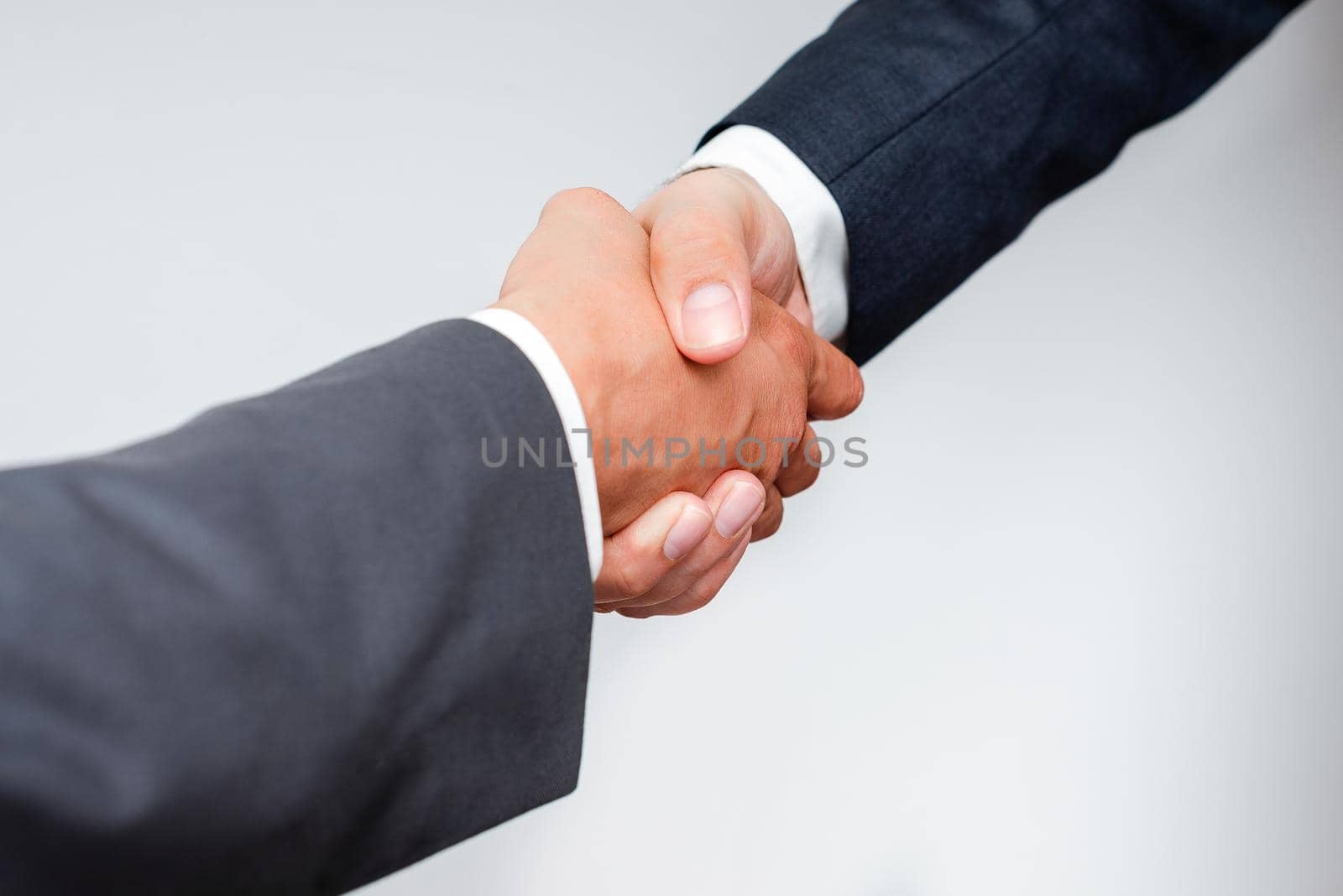 Corporate Businessmen Handshake Indoors.Two People Professionally Well Dressed Gesturing Togetherness.Working Colleague Partners Sign Deal In Agreement To Contract by nialowwa