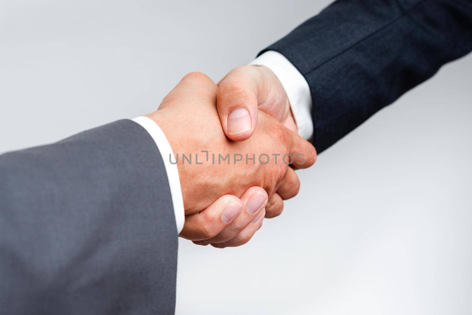 Corporate Businessmen Handshake Indoors.Two People Professionally Well Dressed Gesturing Togetherness.Working Colleague Partners Sign Deal In Agreement To Contract by nialowwa