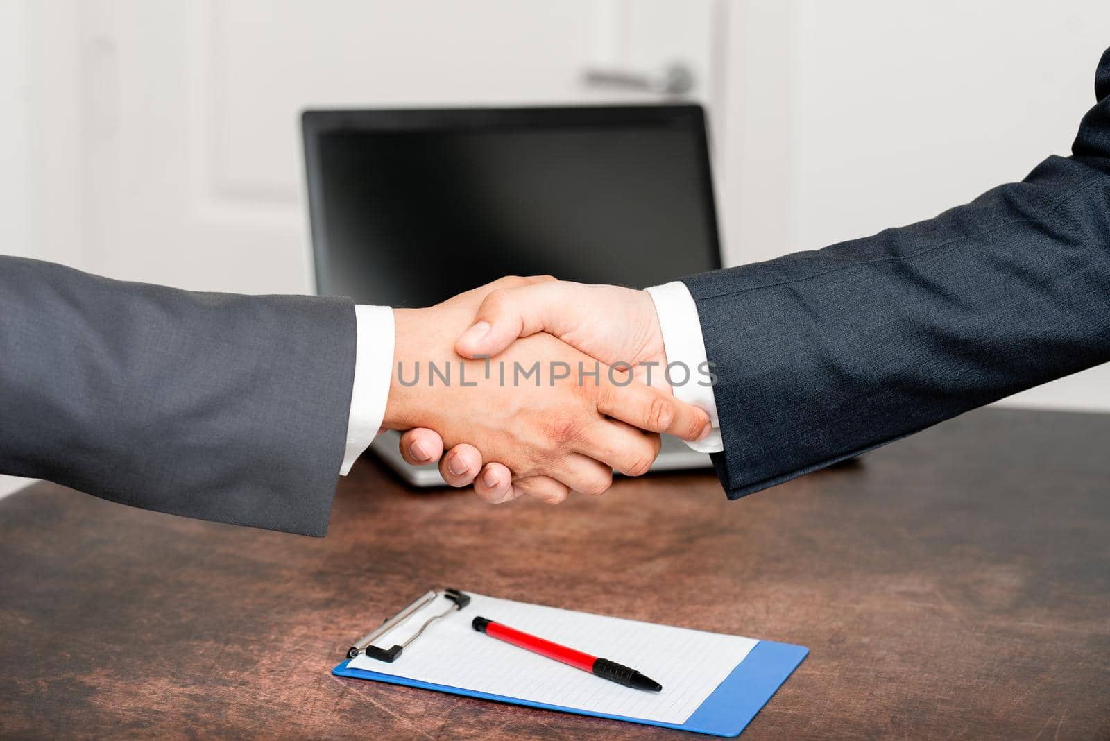 Corporate Businessmen Handshake Indoors.Two People Professionally Well Dressed Gesturing Togetherness.Working Colleague Partners Sign Deal In Agreement To Contract by nialowwa