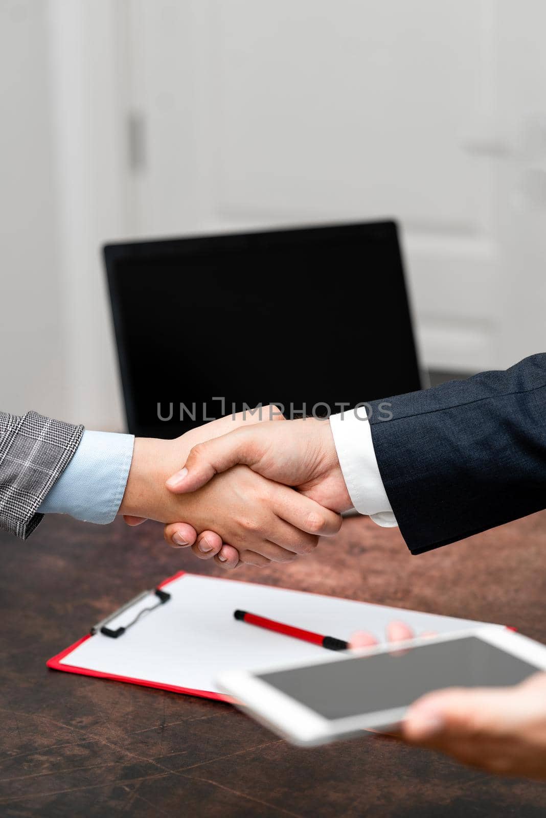 Corporate Businessmen Handshake Indoors.Two People Professionally Well Dressed Gesturing Togetherness.Working Colleague Partners Sign Deal In Agreement To Contract by nialowwa