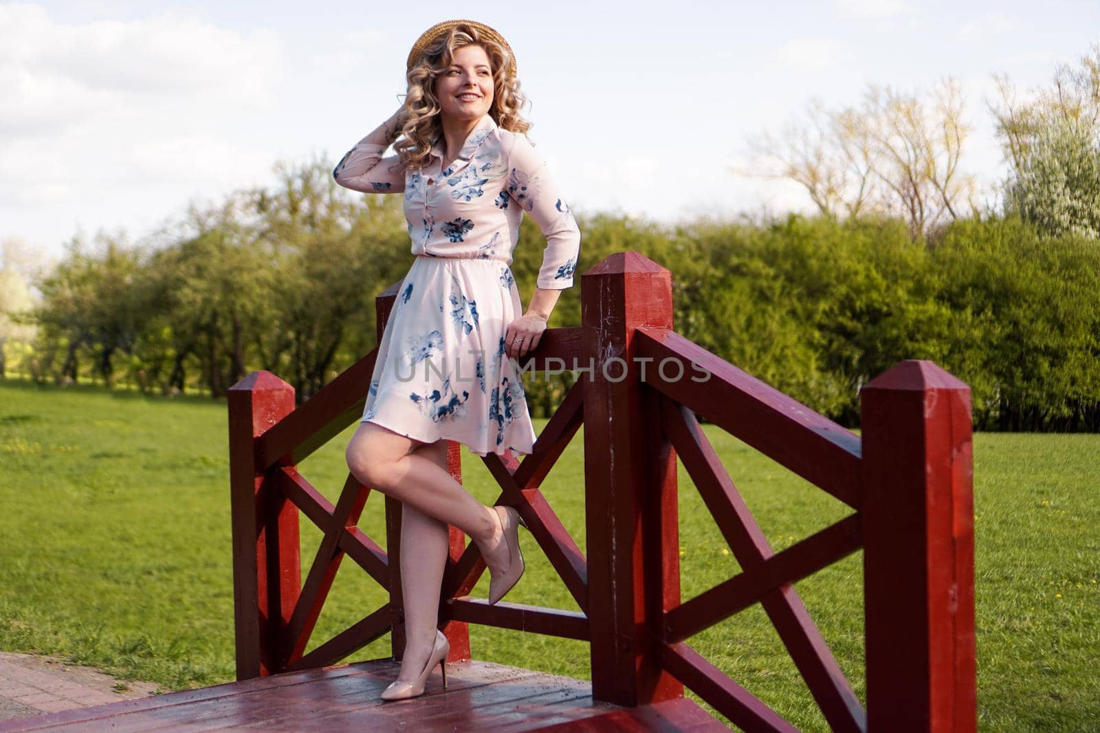 Beautiful woman in summer dress and straw hat stands on birch bridge in the park by natali_brill