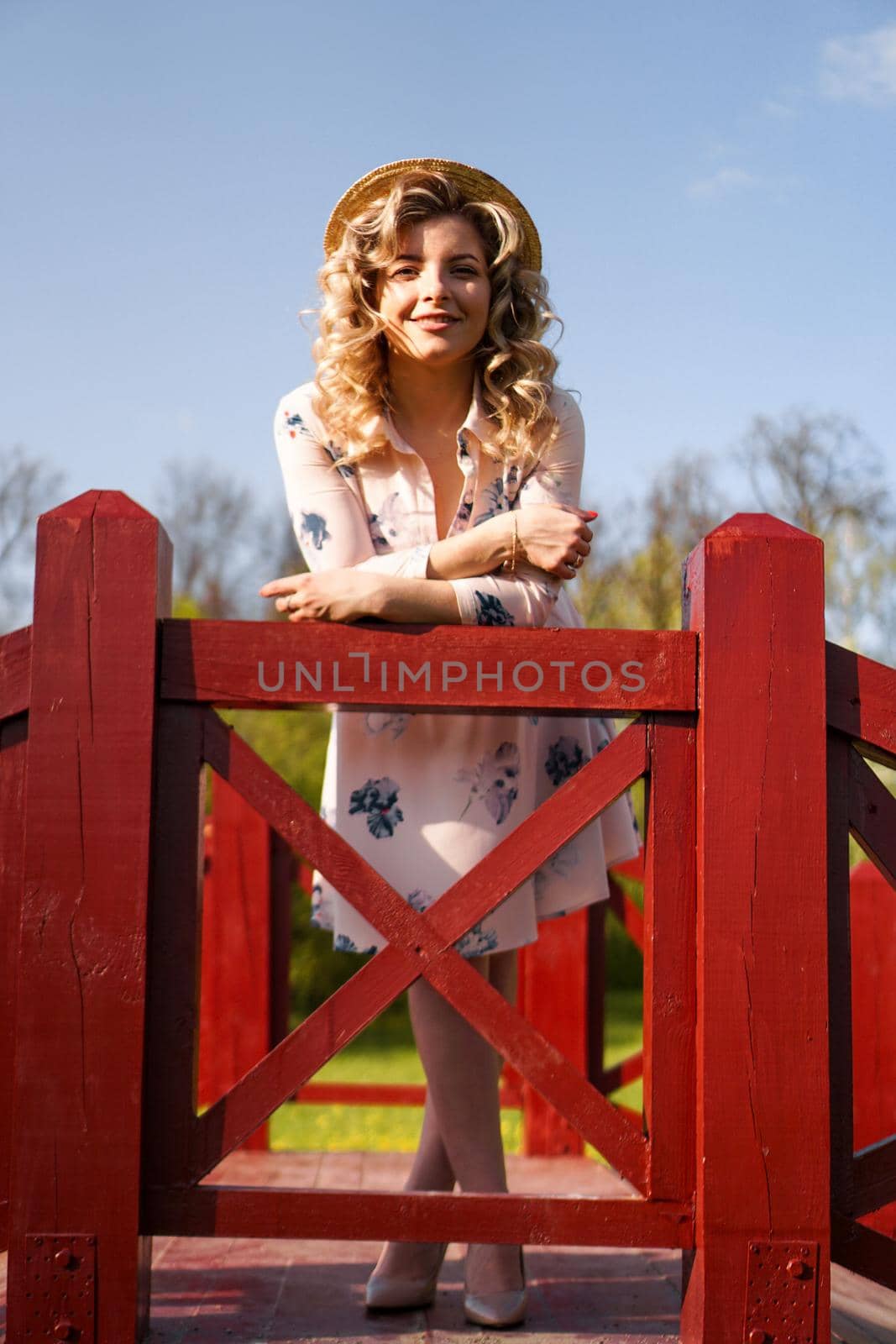 Beautiful woman in a white summer dress and a straw hat stands on a birch bridge in the park