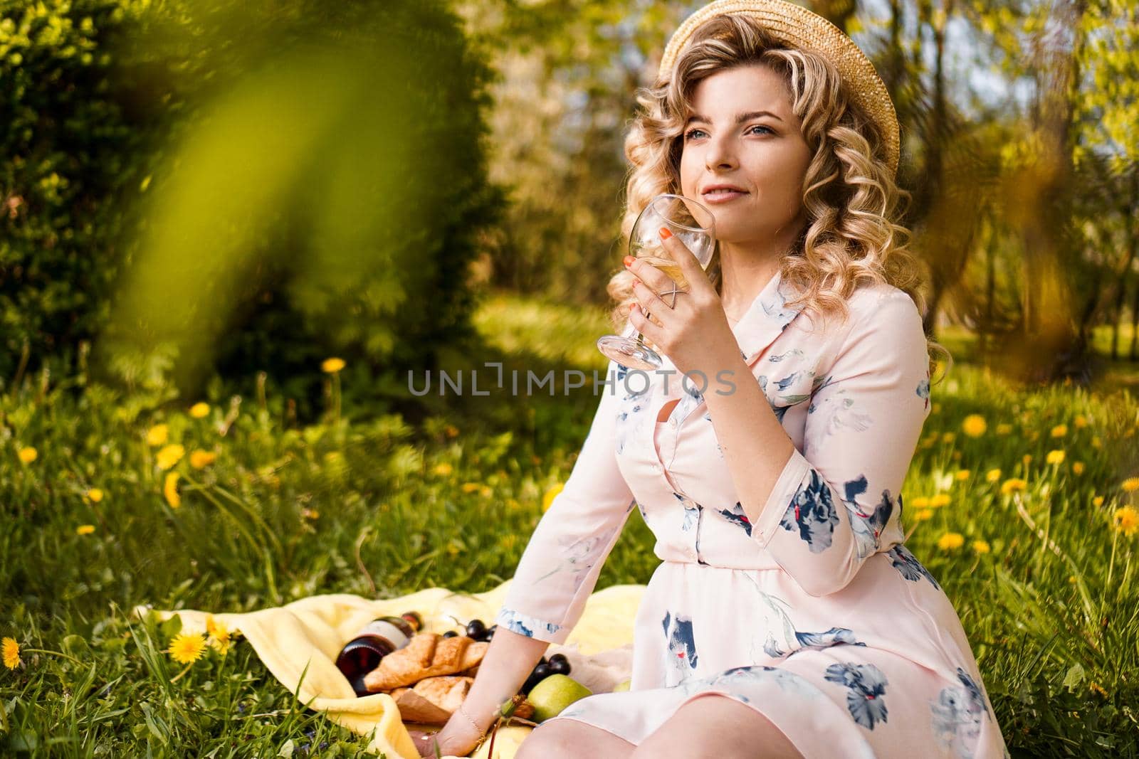 Beautiful young woman with blonde hair in straw hat drinks wine in the garden by natali_brill