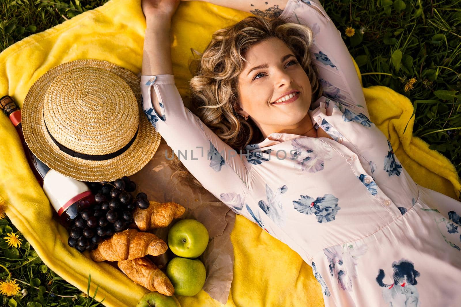 Young girl in hat lying on the plaid with wine and fresh food. Picnic. Natural light