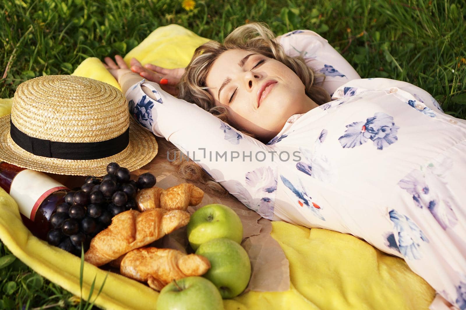 Young girl lying on the plaid with wine and fresh food. Picnic. Natural light