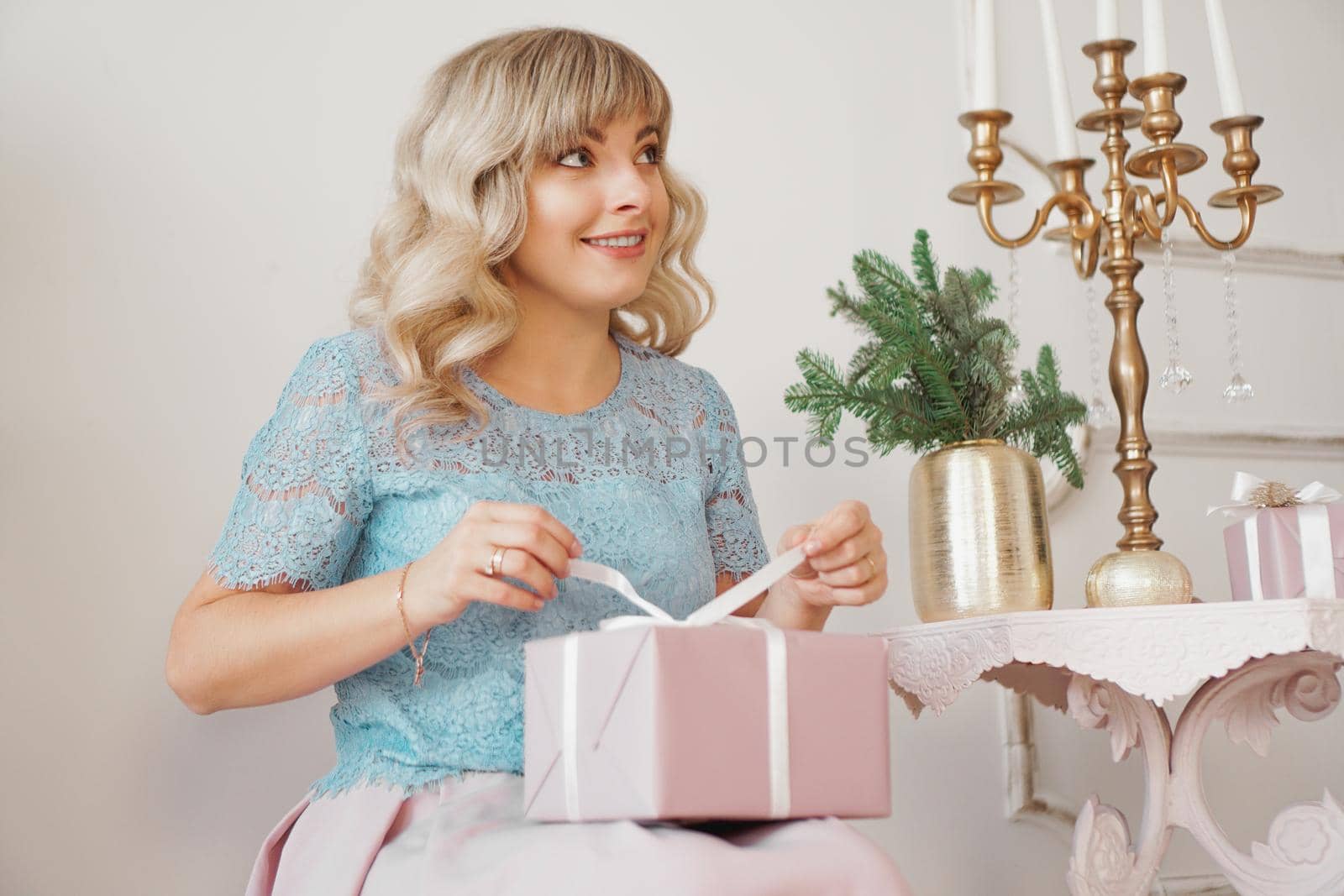 Cute positive woman near Christmas tree, opening gift in pink box